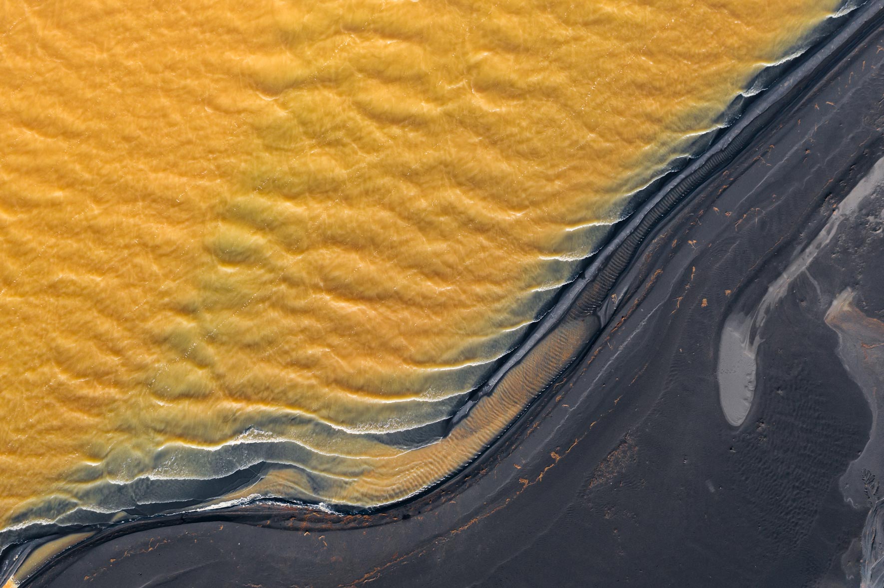 Aerial photograph of yellow river with dark shoreline in Iceland