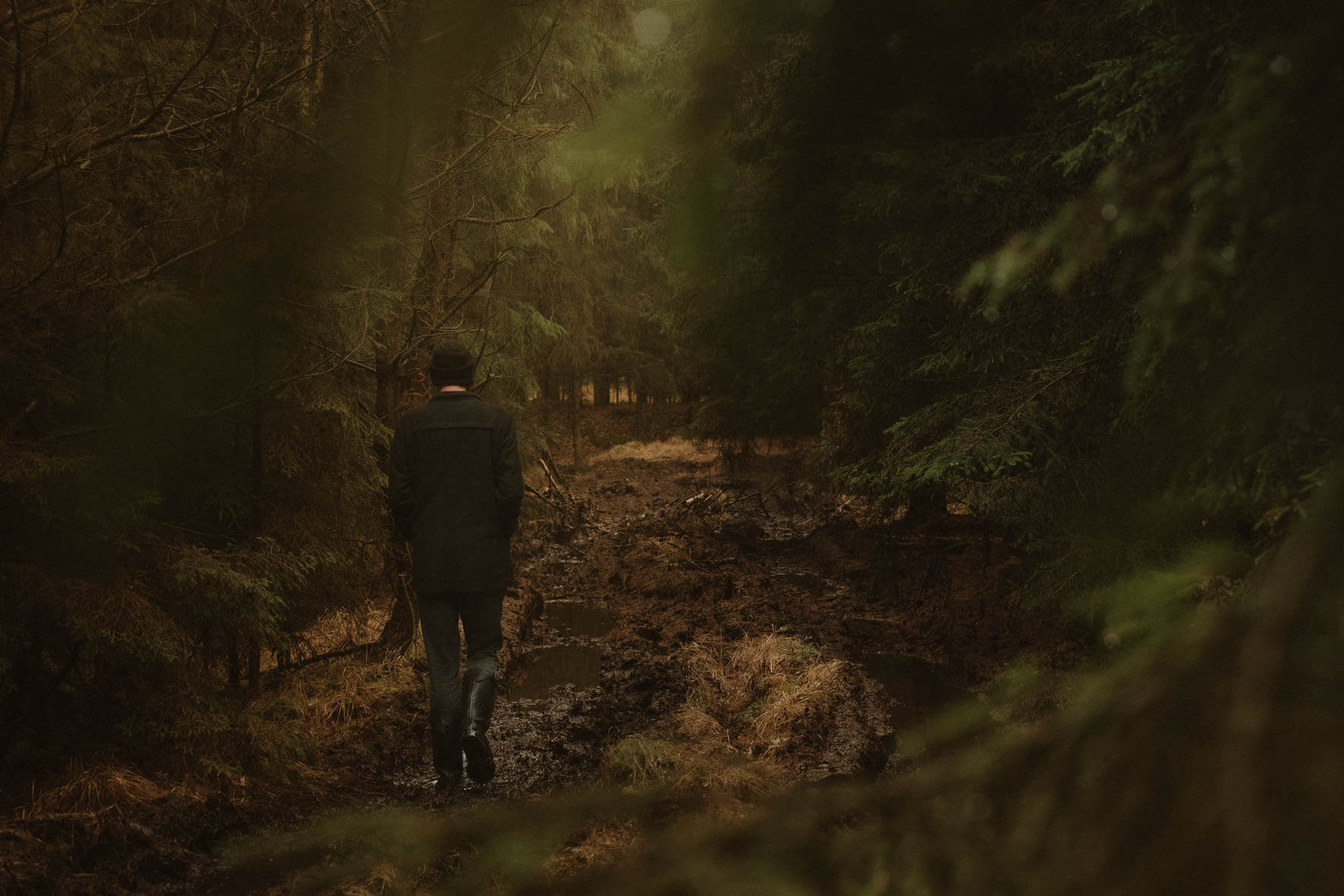 A man walks through a dark autumn forest on a muddy forest path
