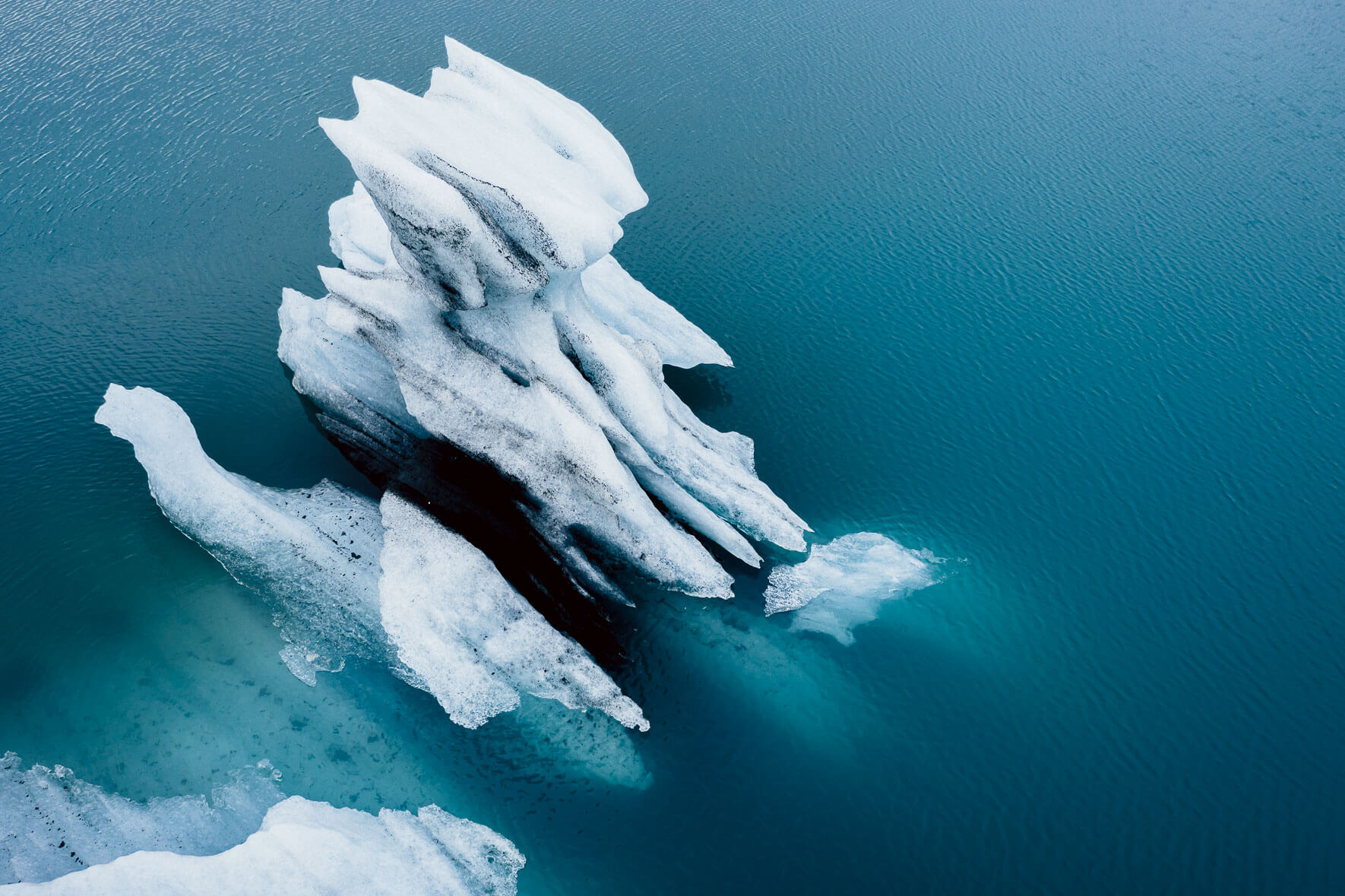Aerial view of iceberg with ash in turquoise glacier lagoon in Iceland