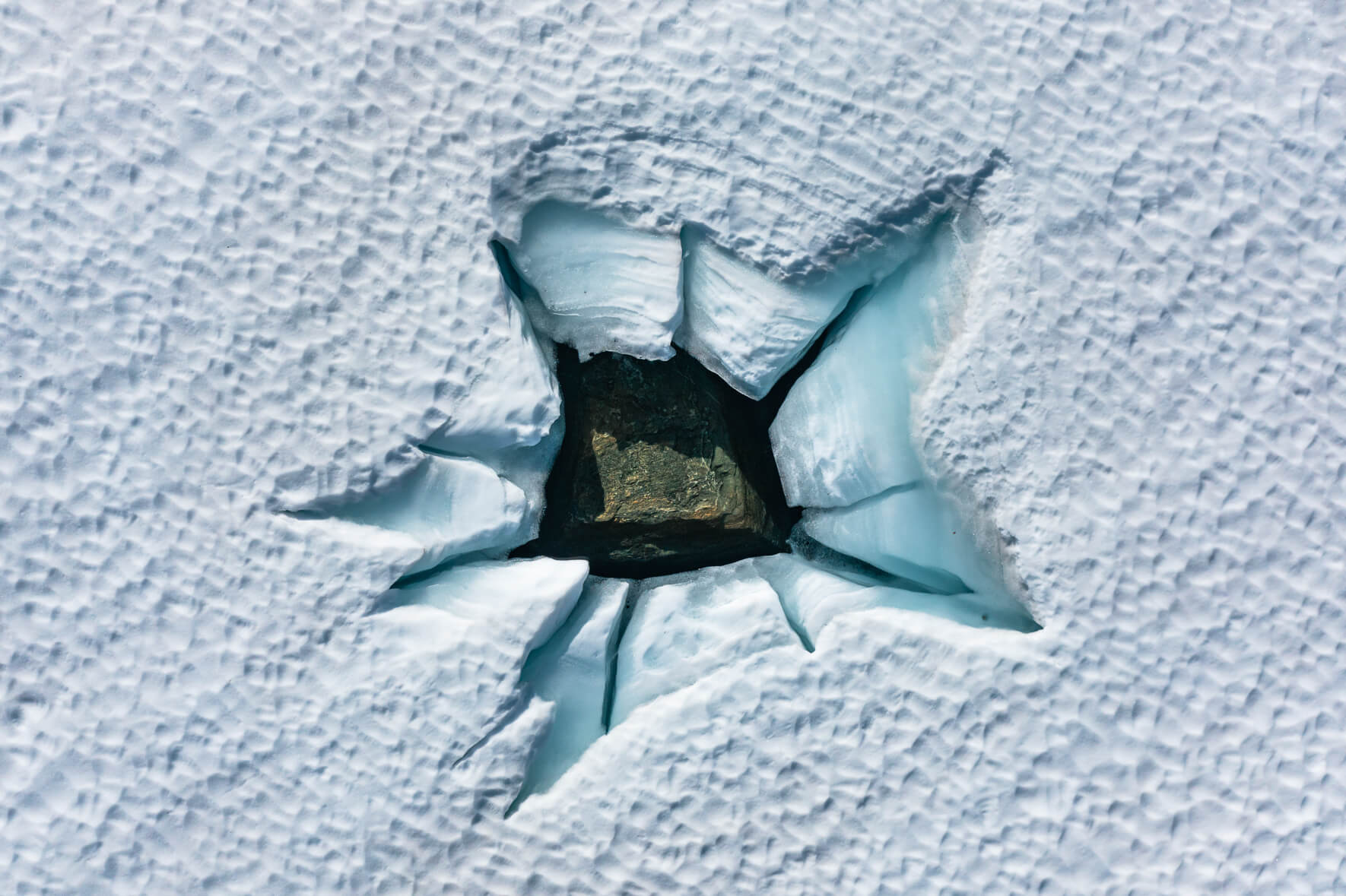 Cracked surface of a snow-covered and frozen lake in Norway with a rock peaking through