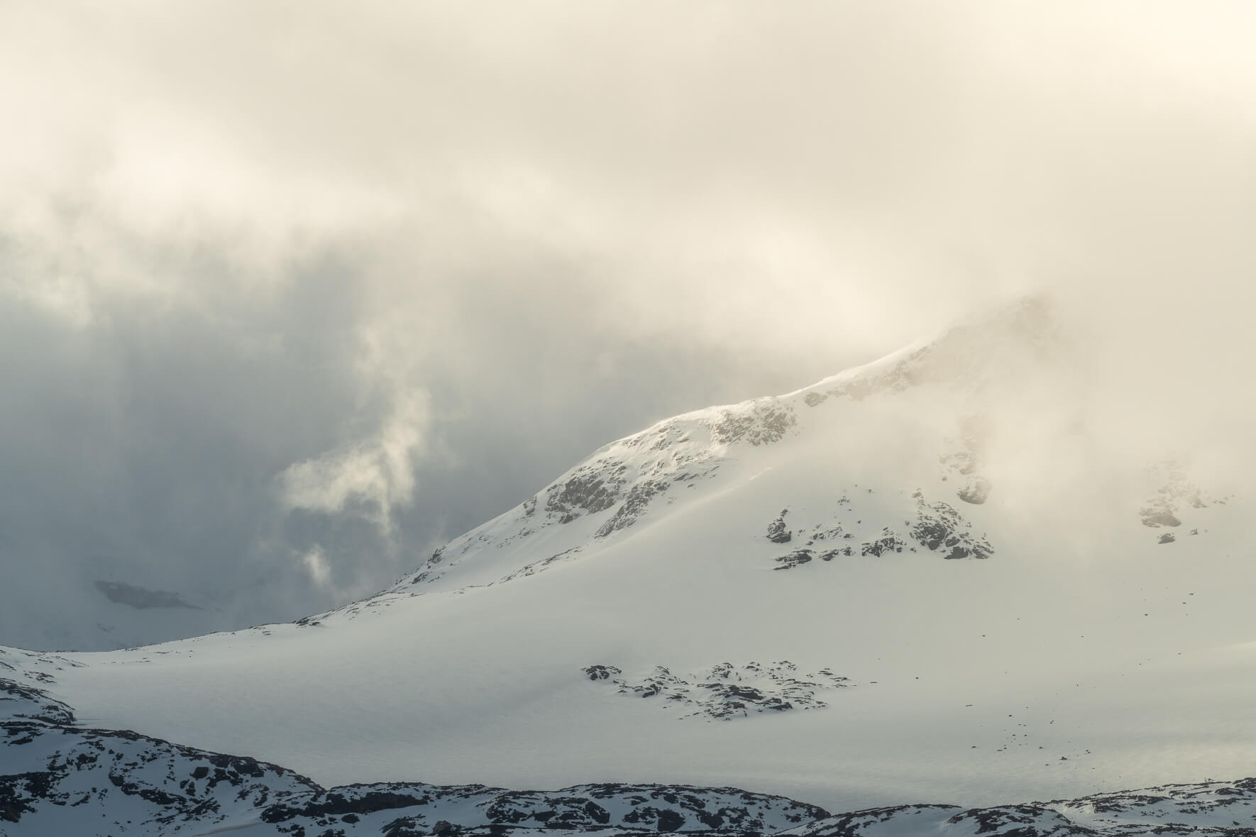 The sun breaks through the clouds over the Sognefjellet mountains and snow-capped rocks
