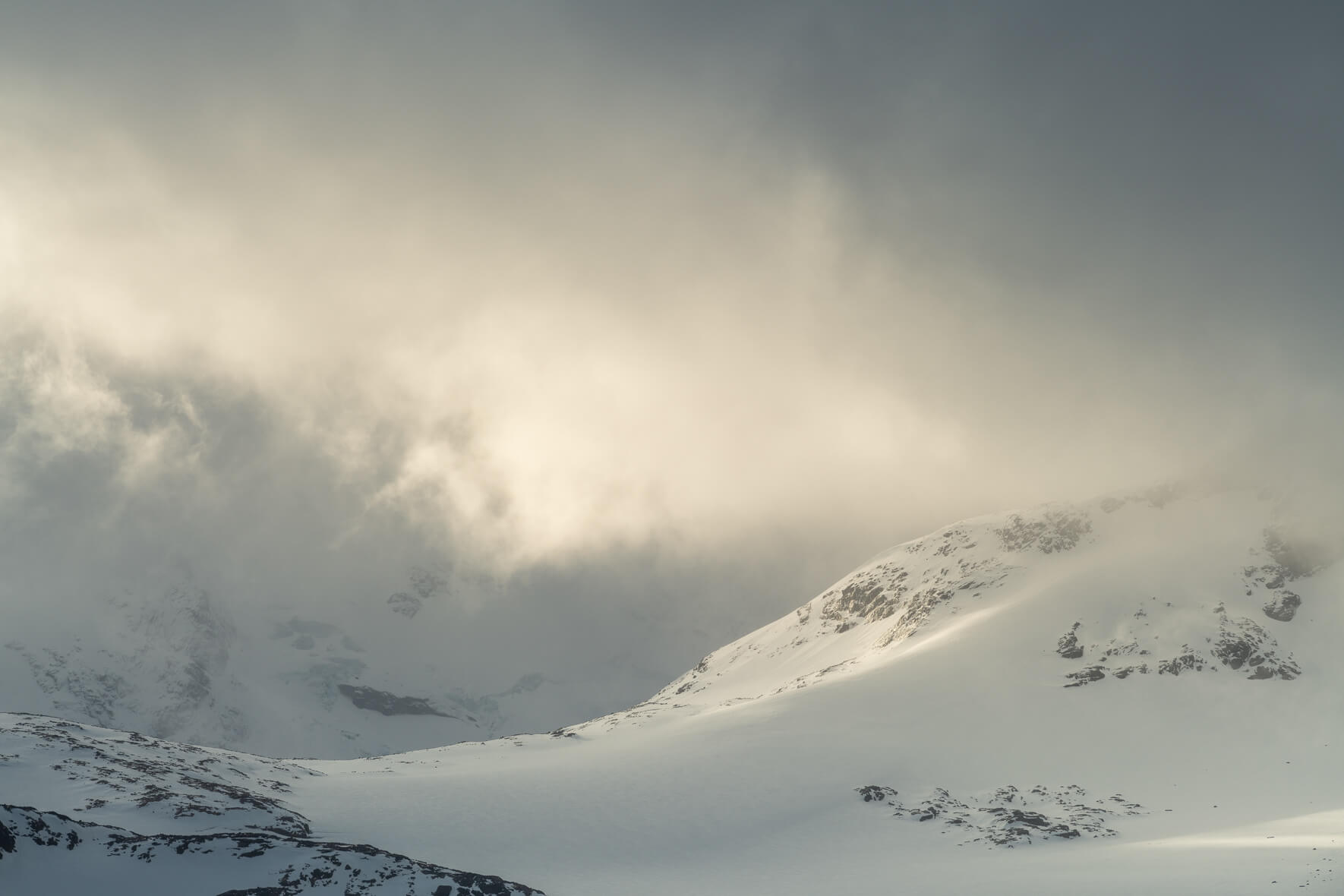 The winter sun breaks through the dark clouds over the Sognefjellet mountains in Norway