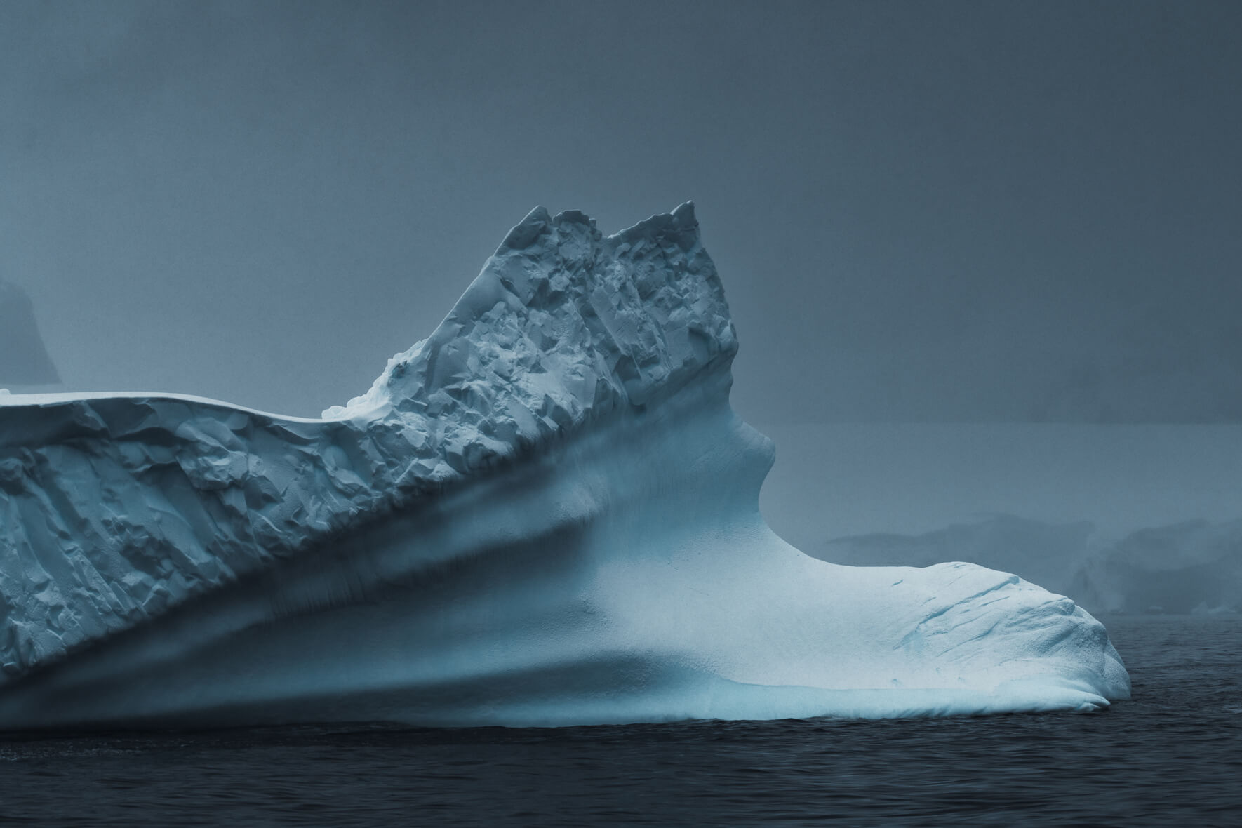 Large iceberg in Antarctica during a snow shower with dark clouds in winter