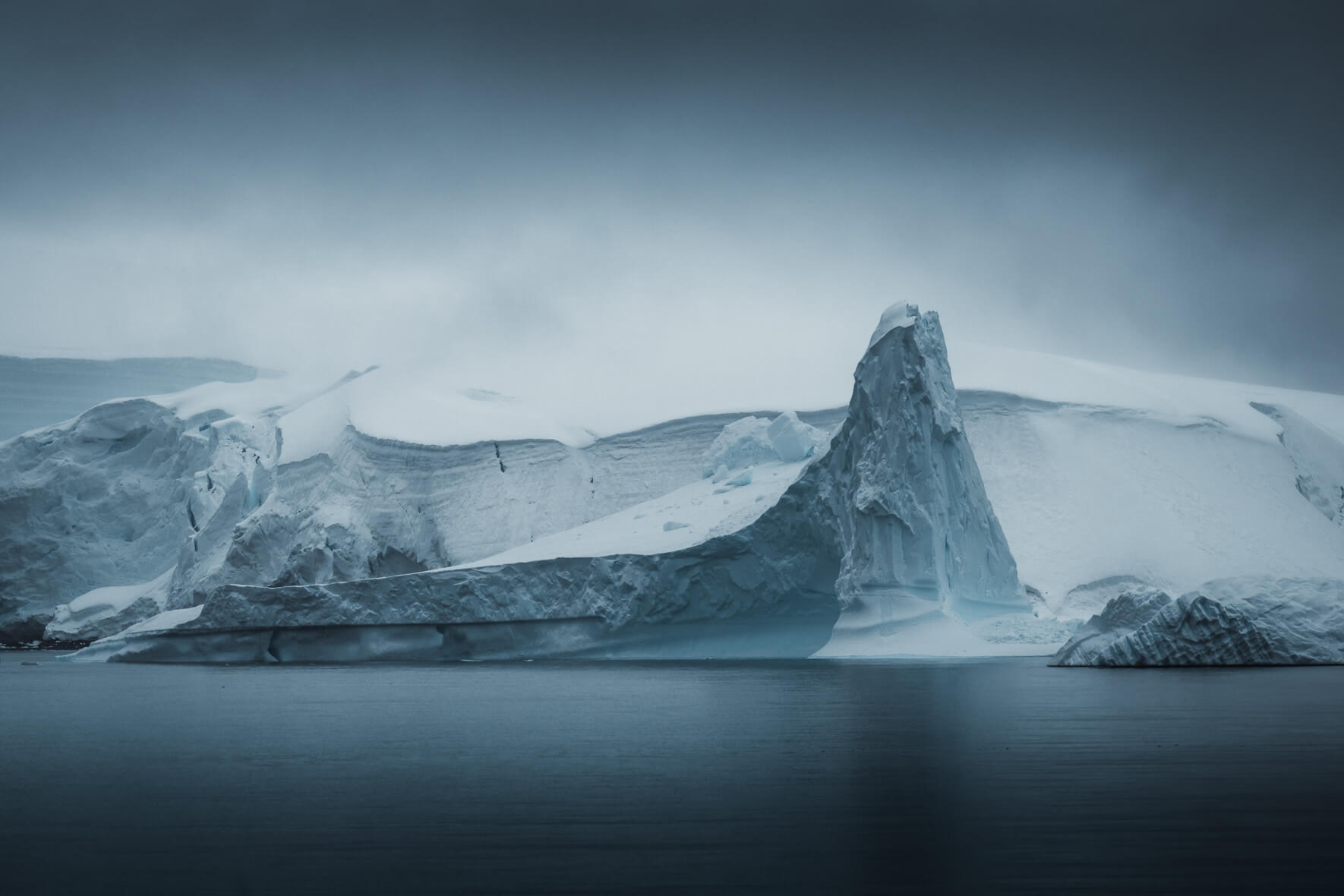 Calm scene with a glacier and icebergs in Antarctica and dark clouds in the sky