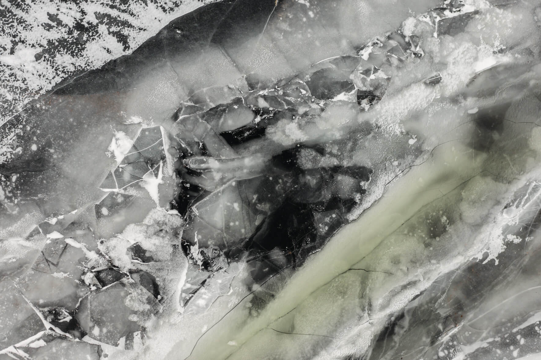 Aerial view of frozen lake with colorful and abstract textures and breaking ice in late winter