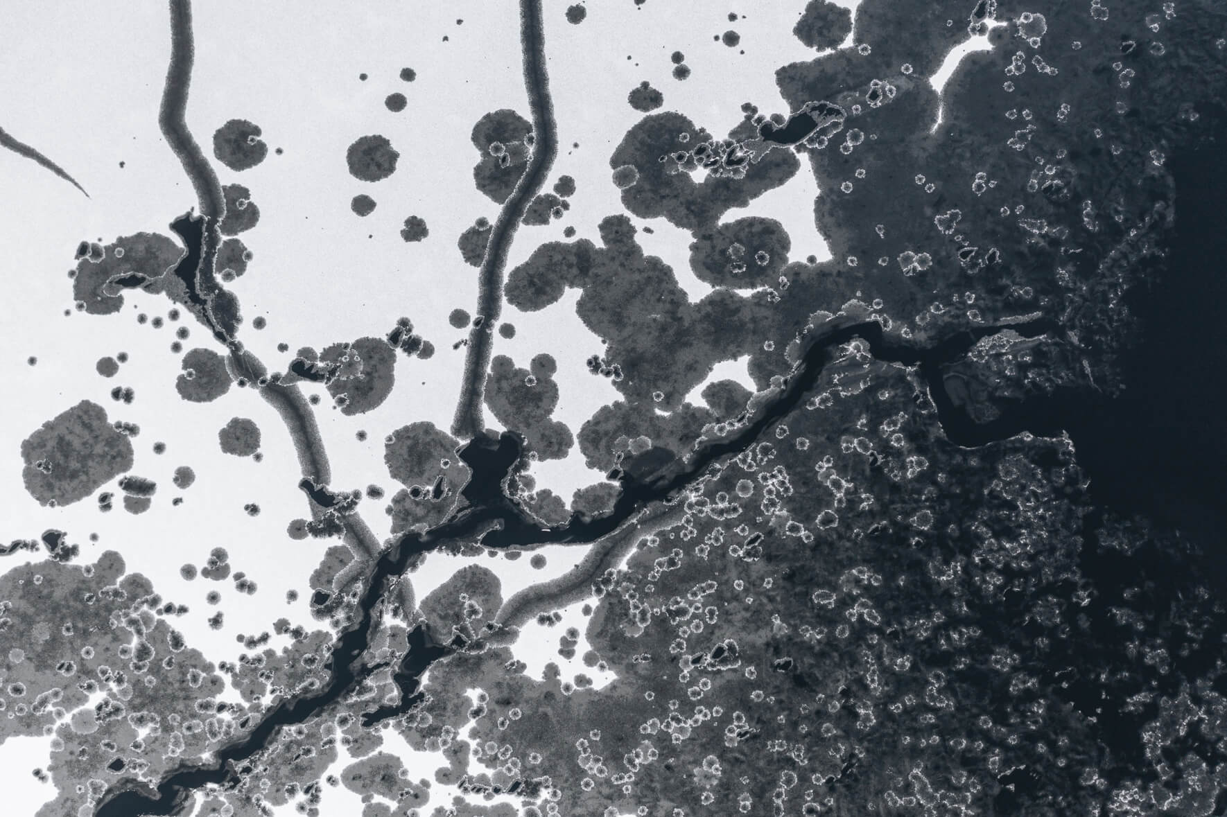 Aerial view of a frozen lake in Norway with windblown snow and various holes in ice due to thawing weather