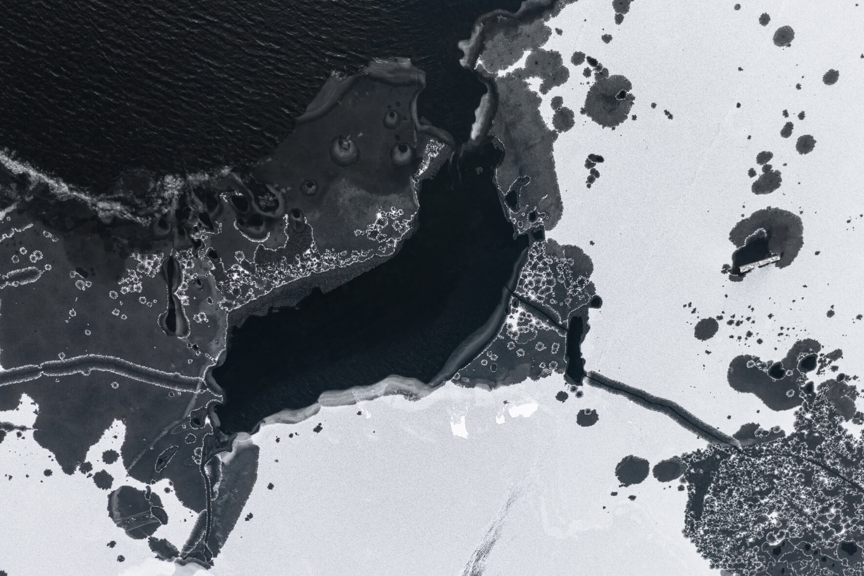 Frozen lake in Norway from an aerial view with various holes in ice due to thawing weather