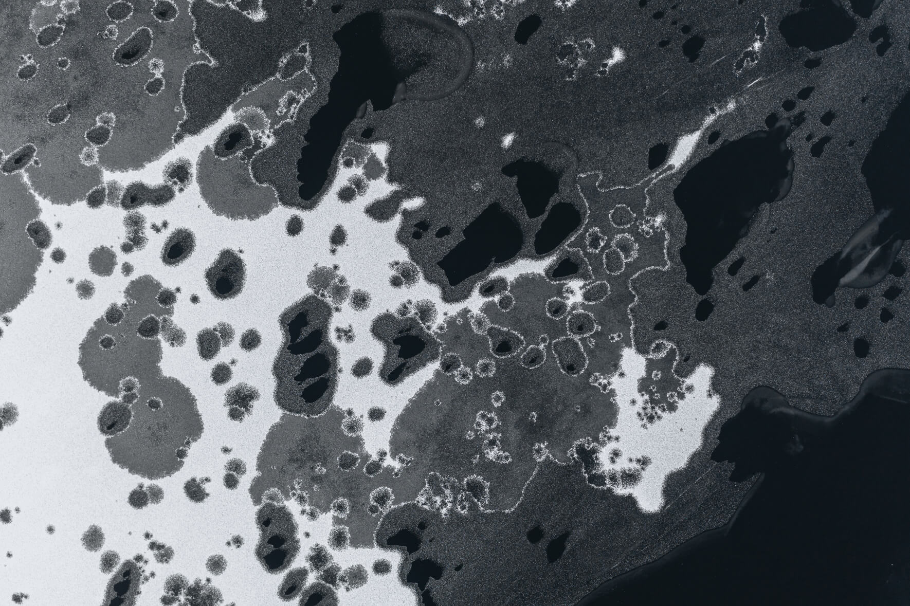 Abstract aerial view of a frozen lake in Norway with large holes in ice due to thawing weather