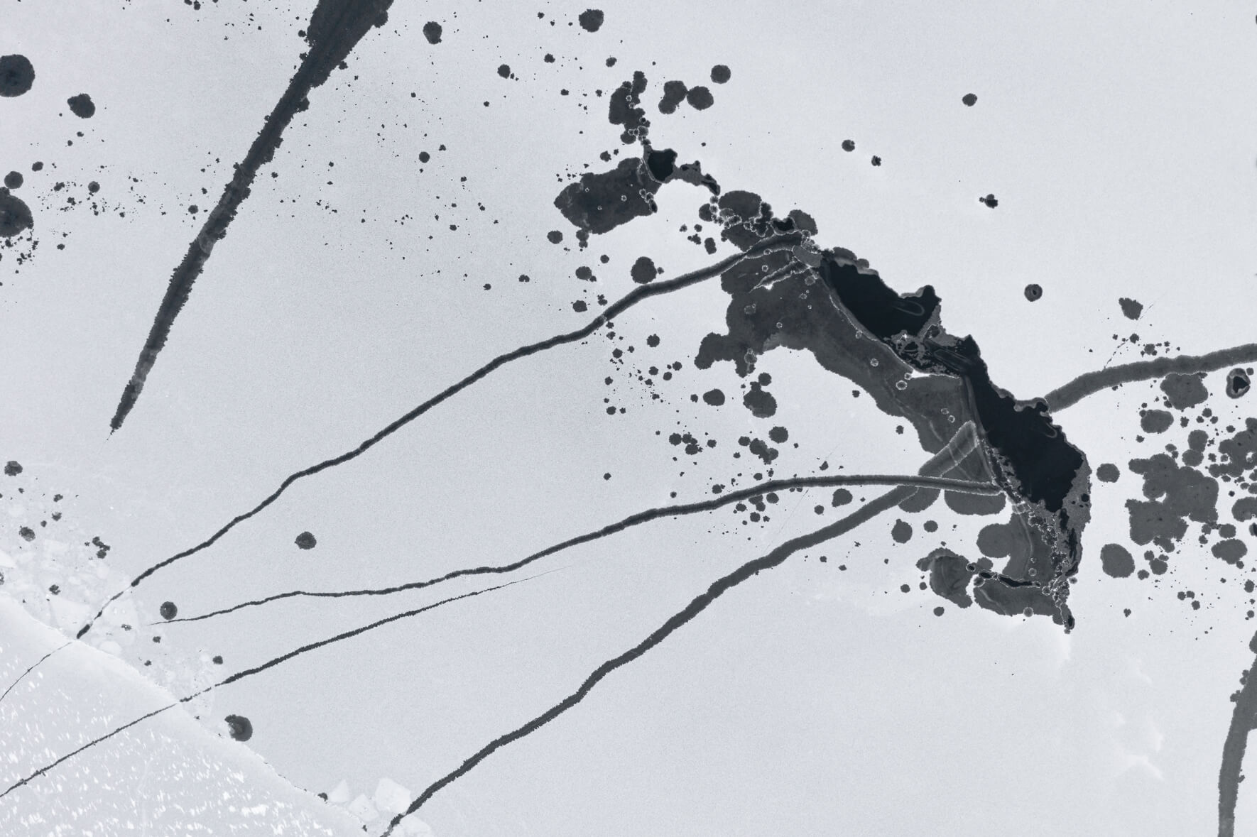 Abstract aerial view of a frozen lake in Norway with cracks and open channels in the ice due to thawing weather