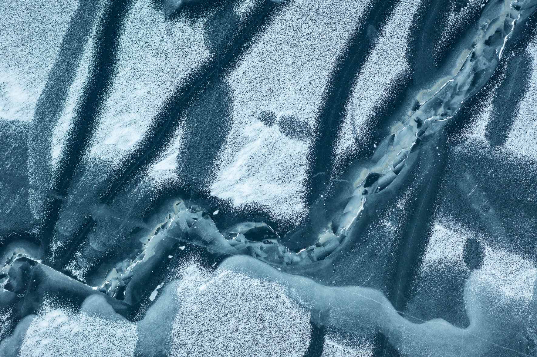 Aerial view of frozen lake Åraksfjorden in Norway with cracks and open channels caused by temperature fluctuations