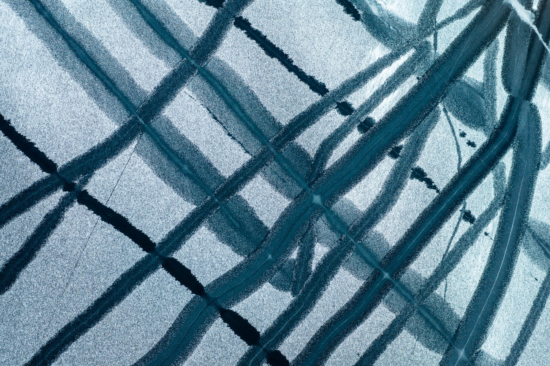 Drone view of a frozen lake in Norway with cracks and open channels caused by temperature fluctuations