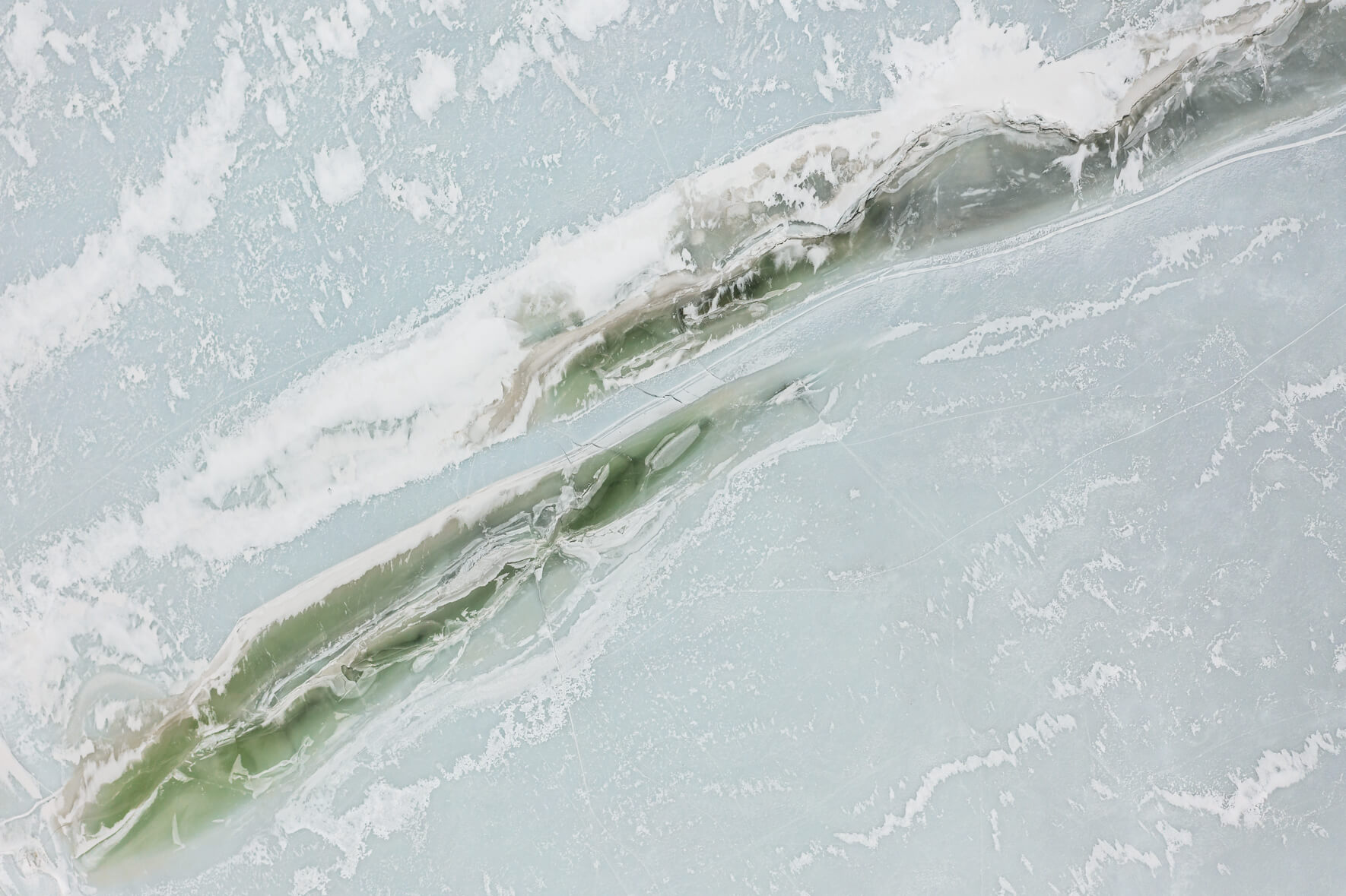 Aerial view of a frozen lake in Norway with cracks in the green colored ice surface