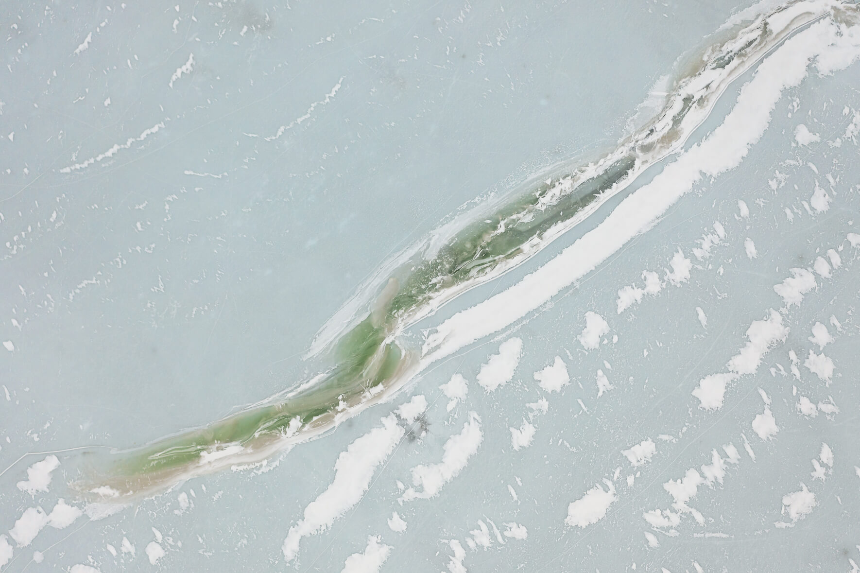 Aerial view of ice of a frozen lake in Norway with a greenish tint due to algae