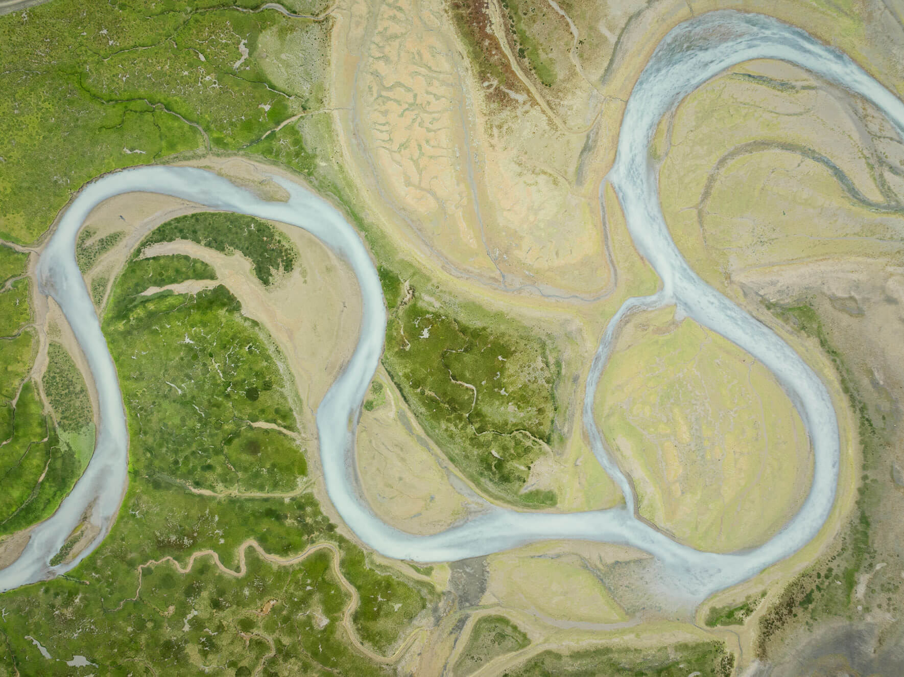Aerial perspective of coastal wetlands in Alaska, showcasing vibrant greens and earthy tones