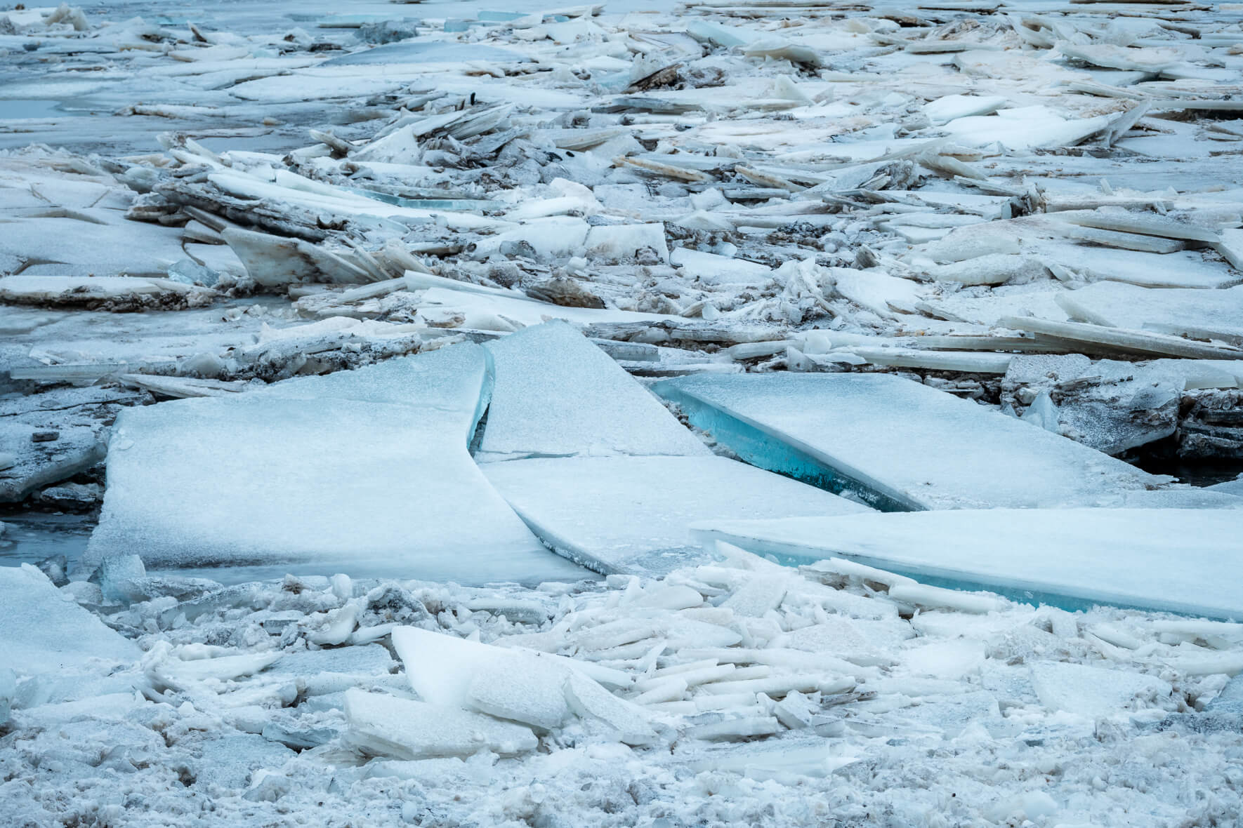 Ice floes piled on top of each other on the banks of a river and turquoise blue ice