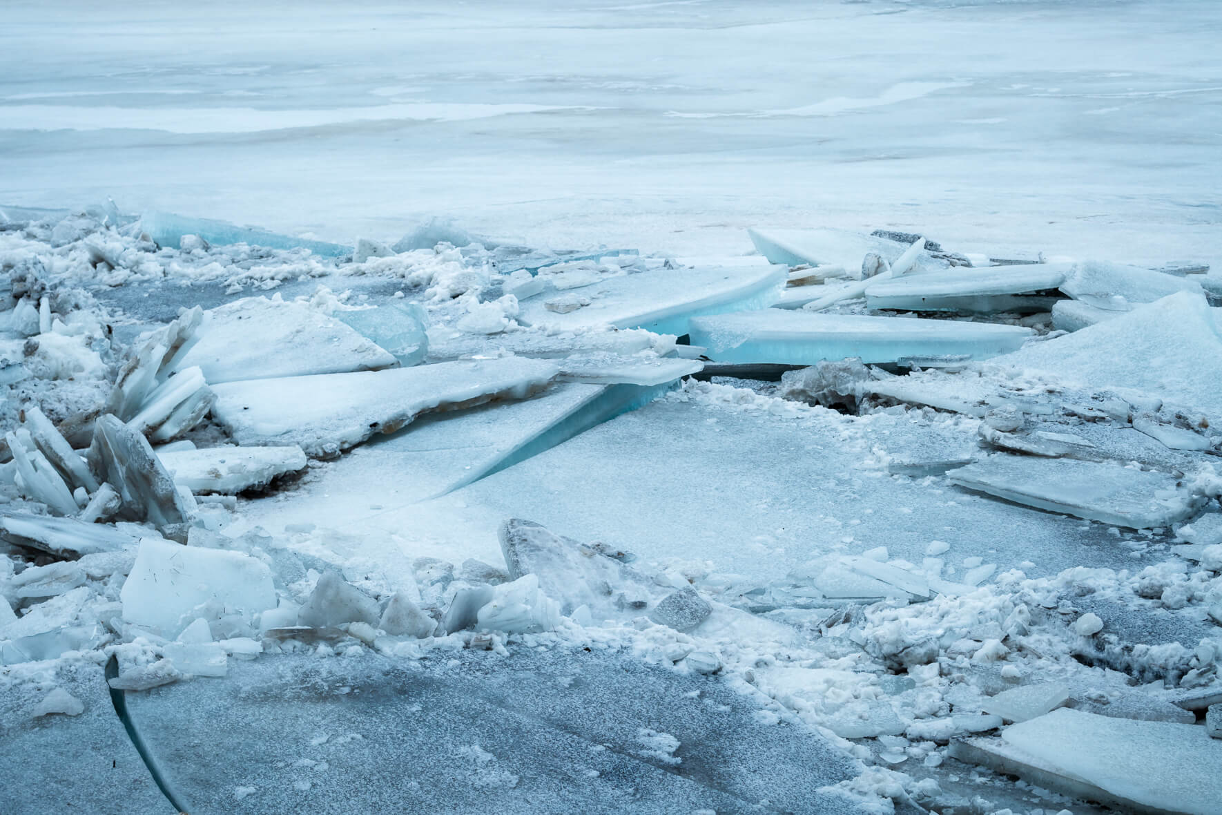 Ice floes piled on top of each other on the banks of a river and turquoise blue ice