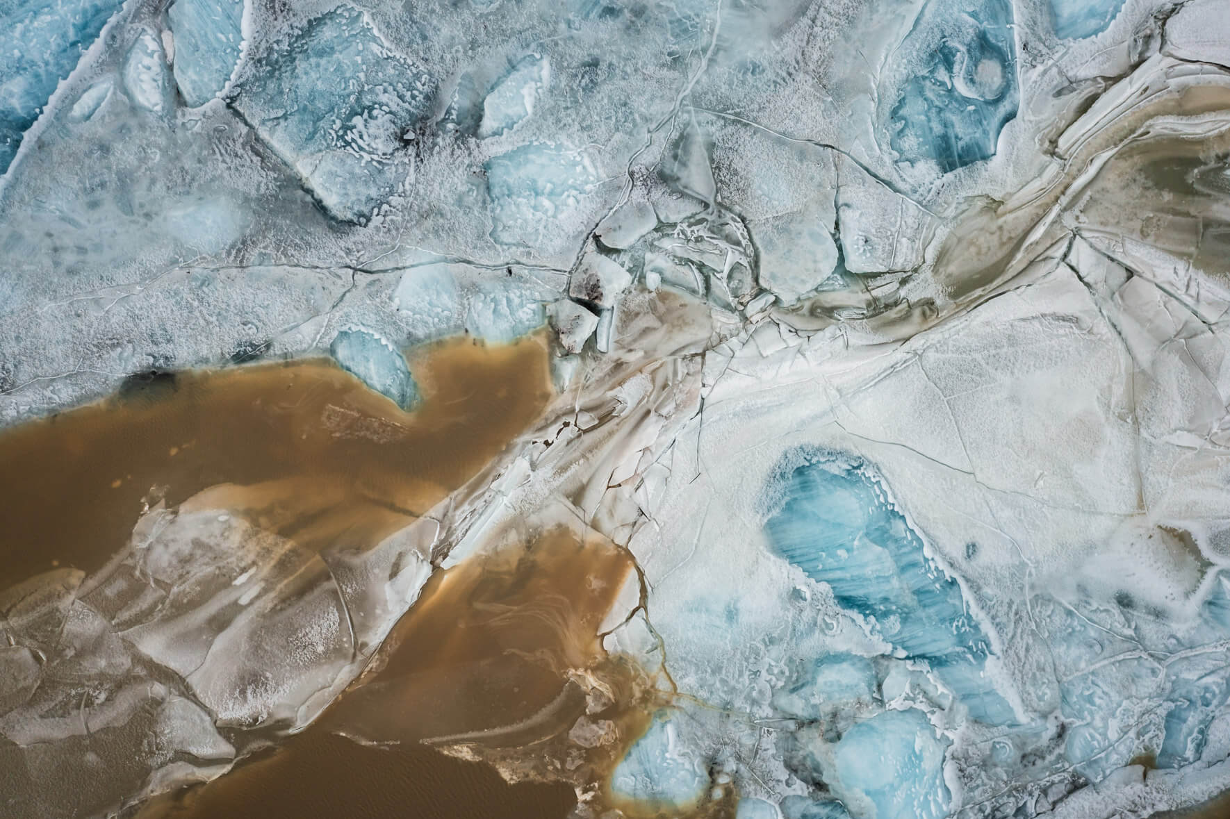 Drone perspective of Svínafellslón in winter, where ice formations reflect blues and earthy tones