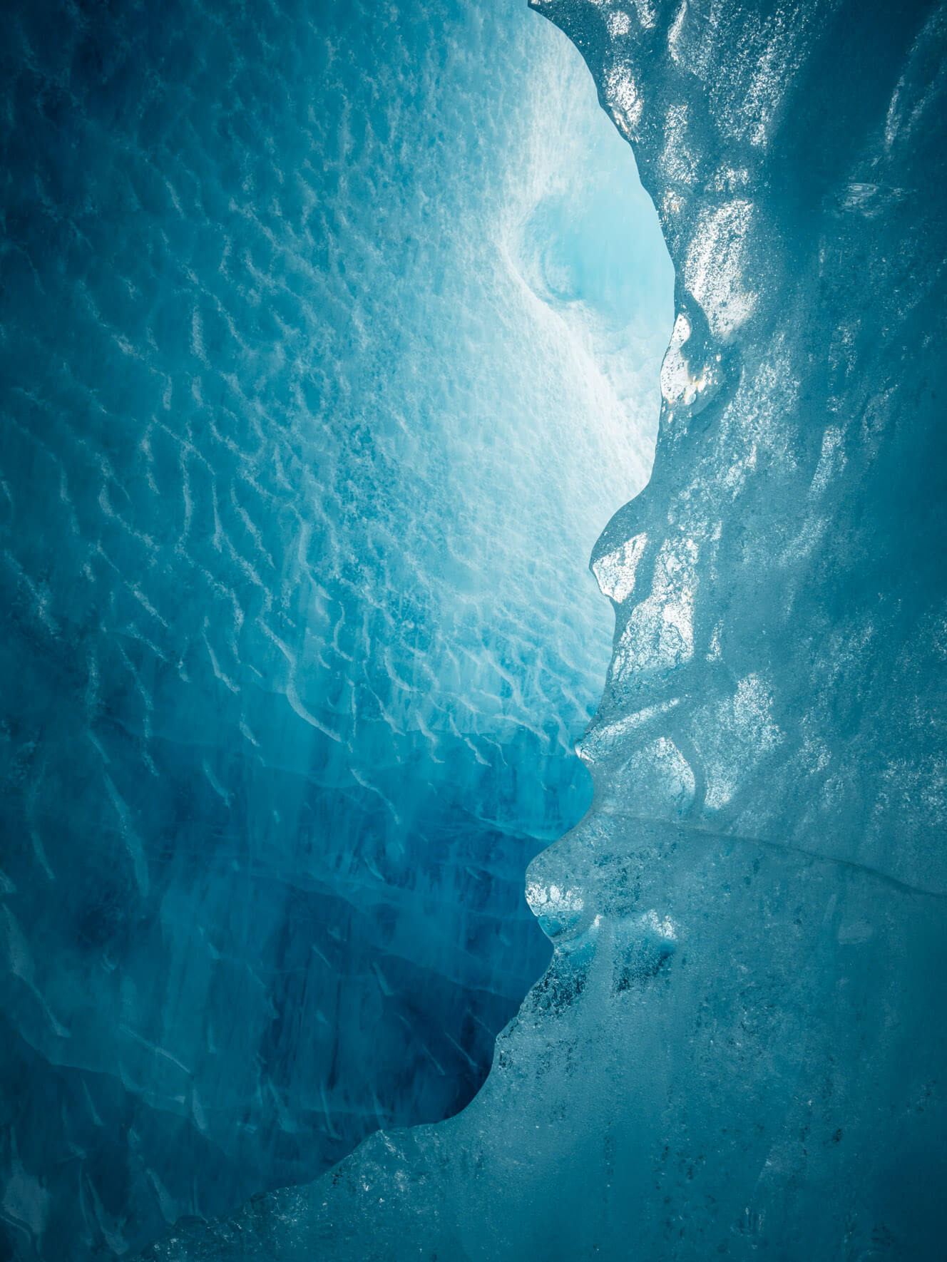 Entrance to a naturally sculpted iceberg tunnel, revealing smooth ice formations and vivid hues