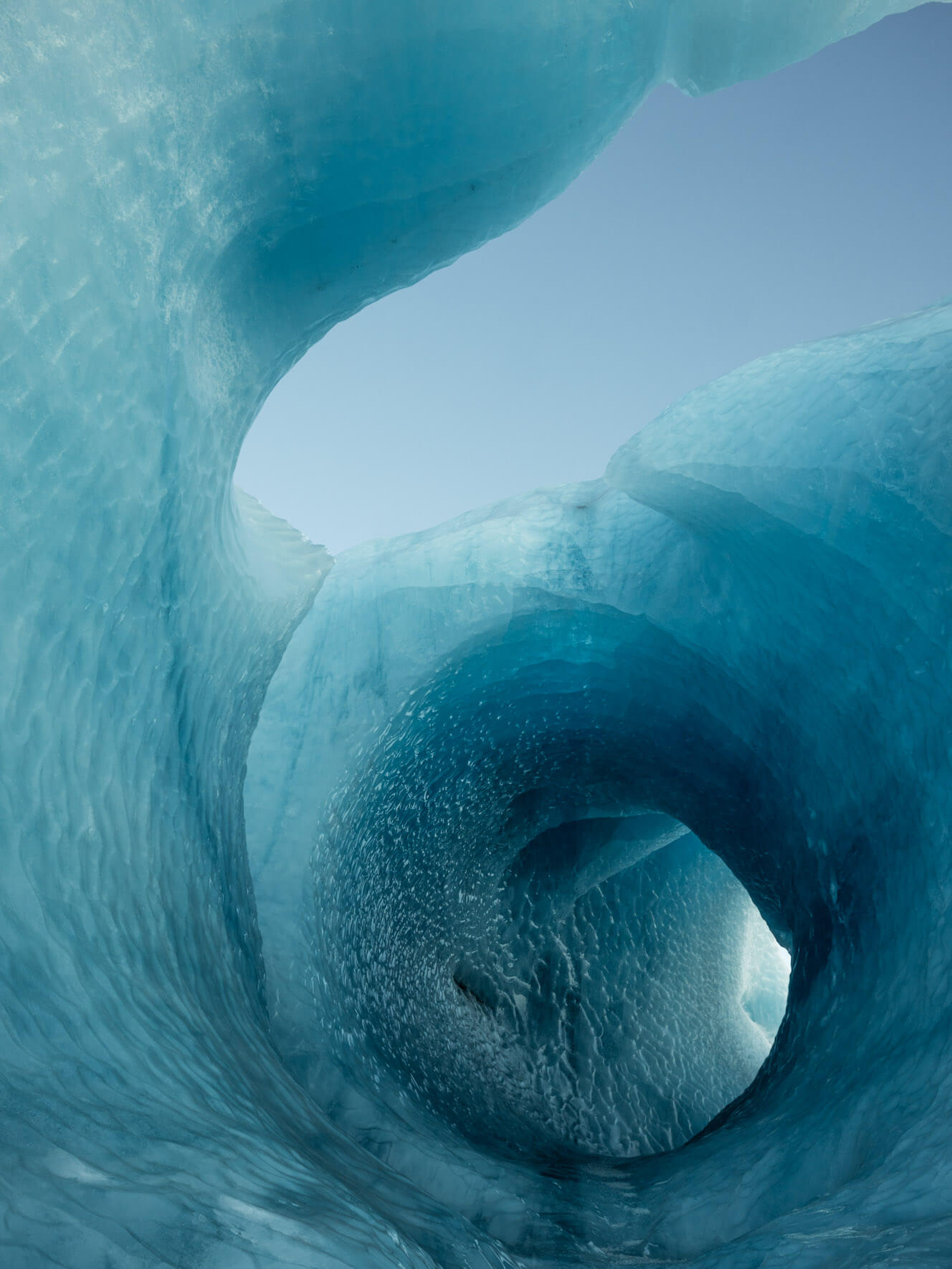 Entrance to a naturally sculpted iceberg tunnel, revealing smooth ice formations and vivid hues
