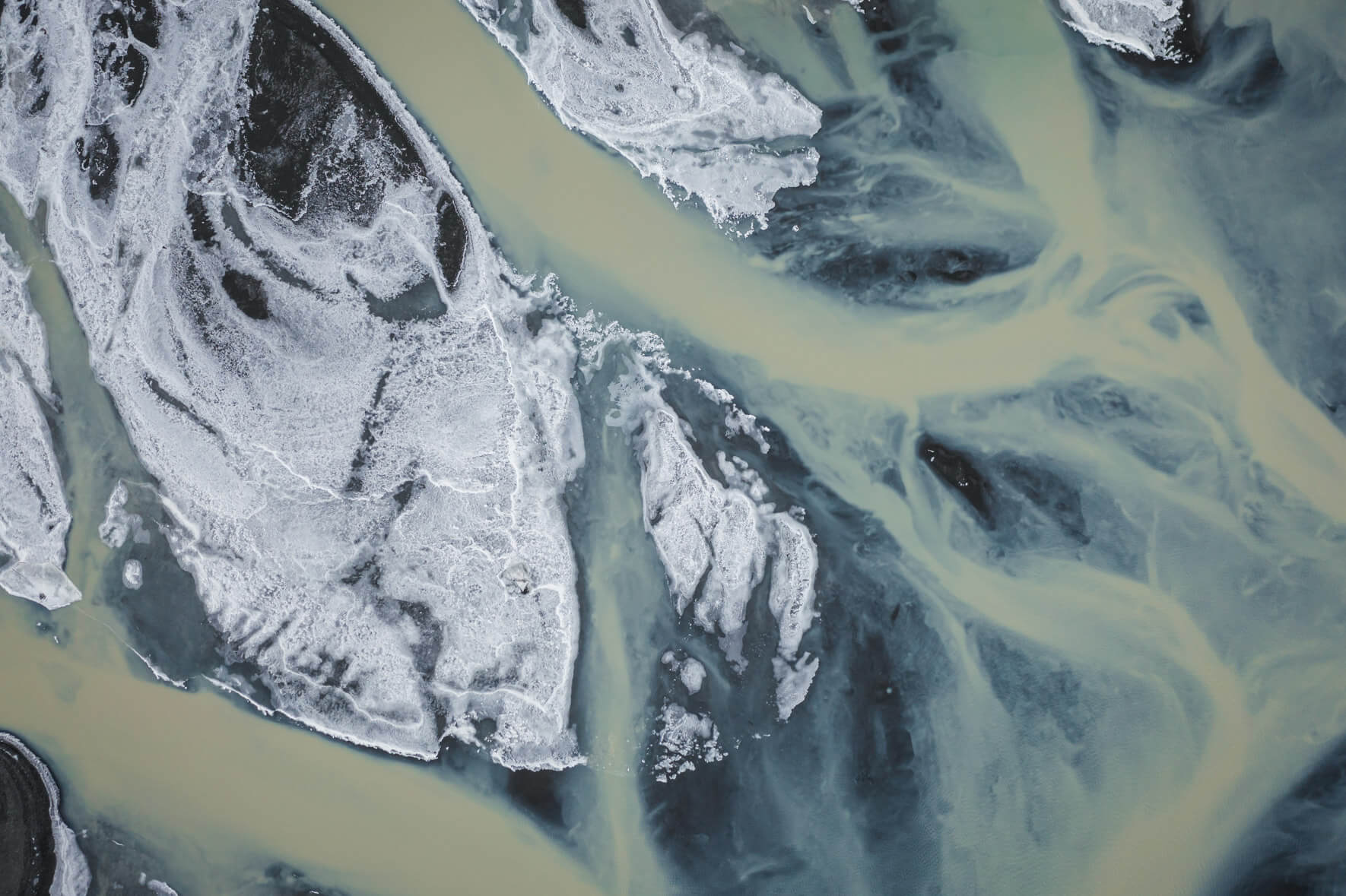 Aerial view of a glacial river on the south coast of Iceland with brown water and ice on the banks