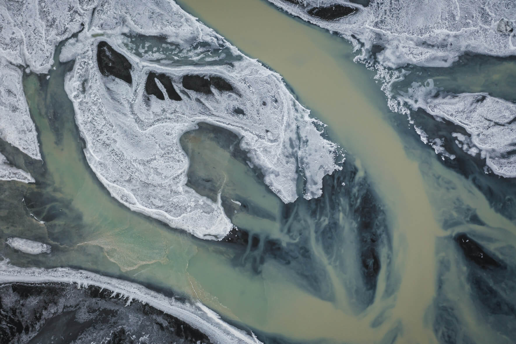 Aerial view of a glacial river on the south coast of Iceland with brown water and ice on the banks
