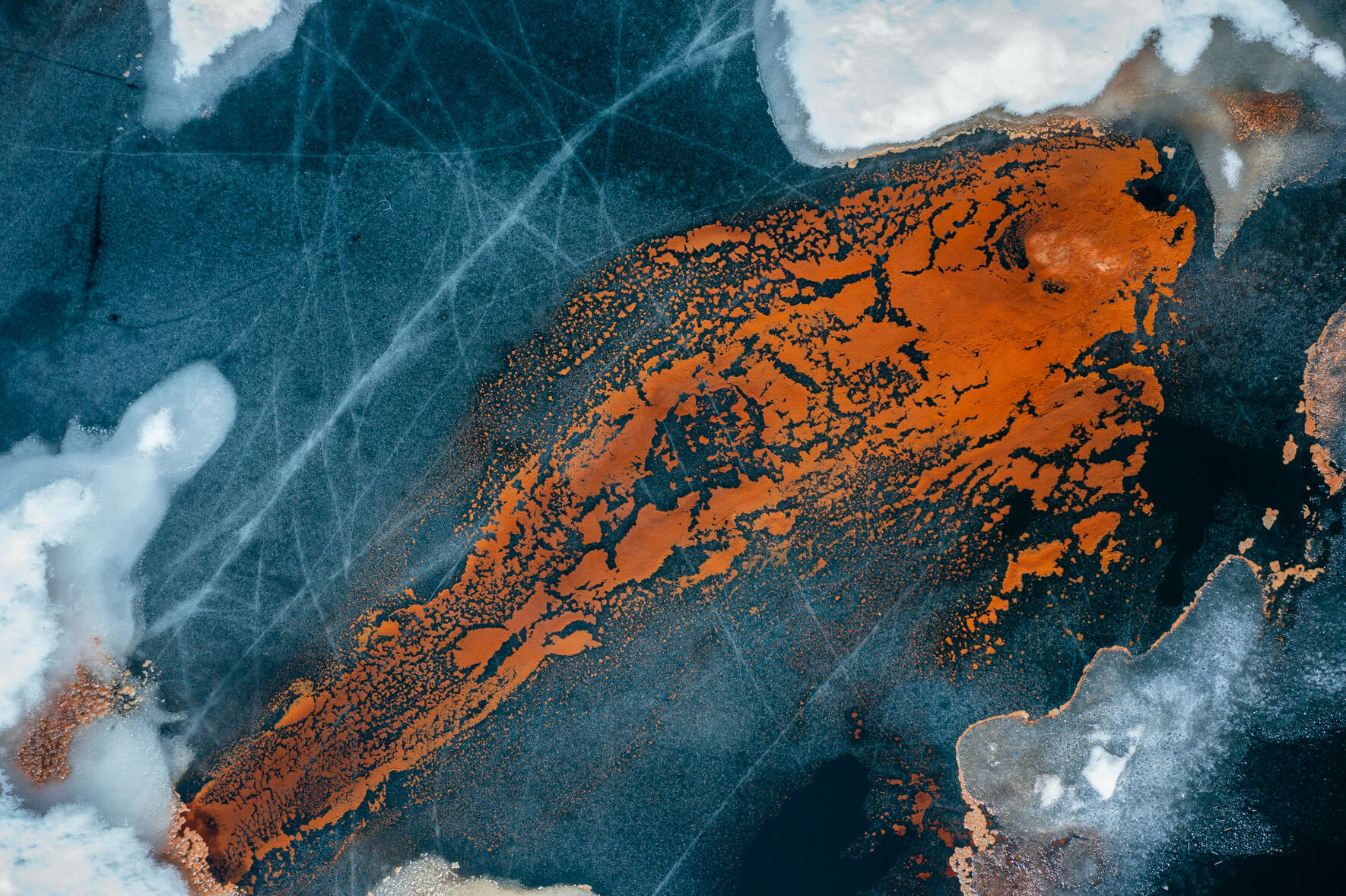 Aerial view of a thawing lake in Norway with ice and red pollen in the shape of a fish