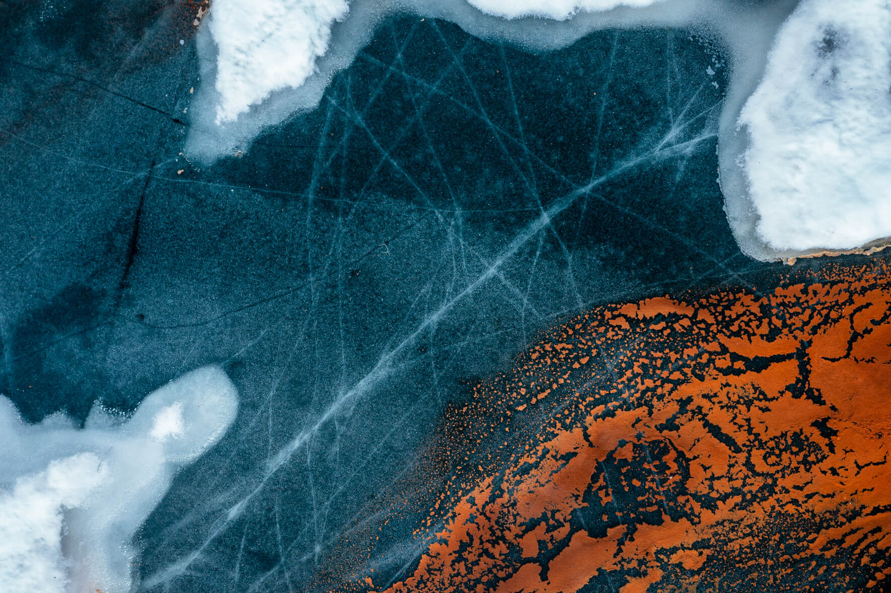Aerial view of a thawing lake in Norway with cracked ice surface and red pollen