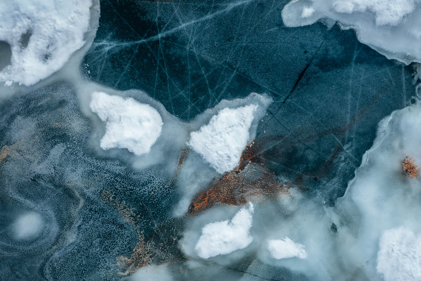 Aerial view of a thawing lake in Norway with cracked ice surface and snow remains