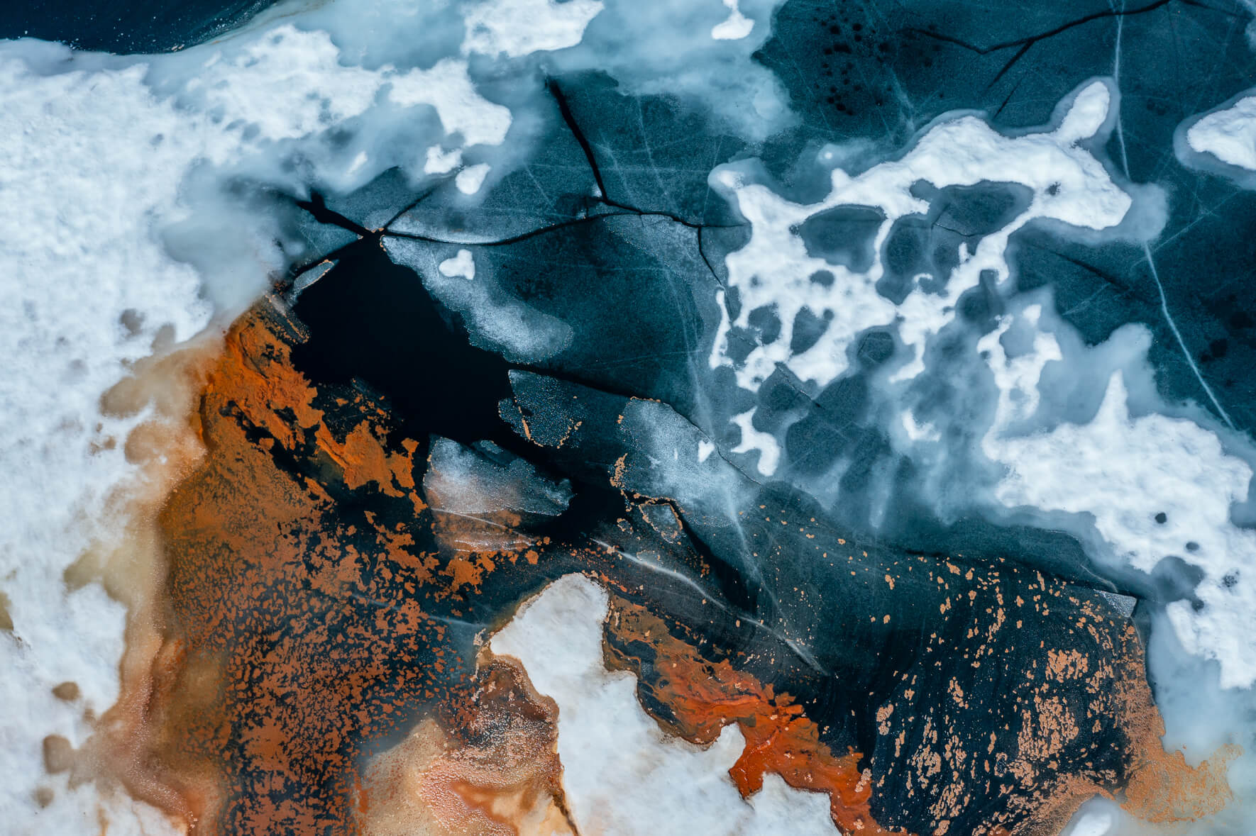 Aerial view of a thawing lake in Norway with cracked ice surface and red pollen from trees