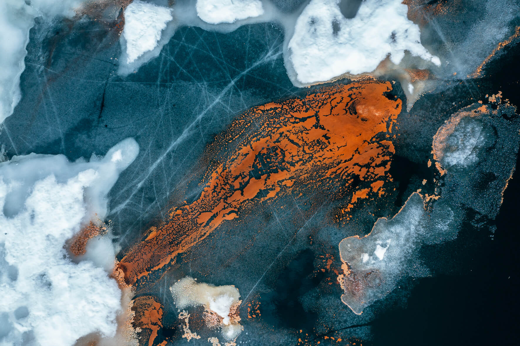 Aerial view of a thawing lake in Norway with cracked ice surface and remnants of snow as well as red pollen in the shape of a fish