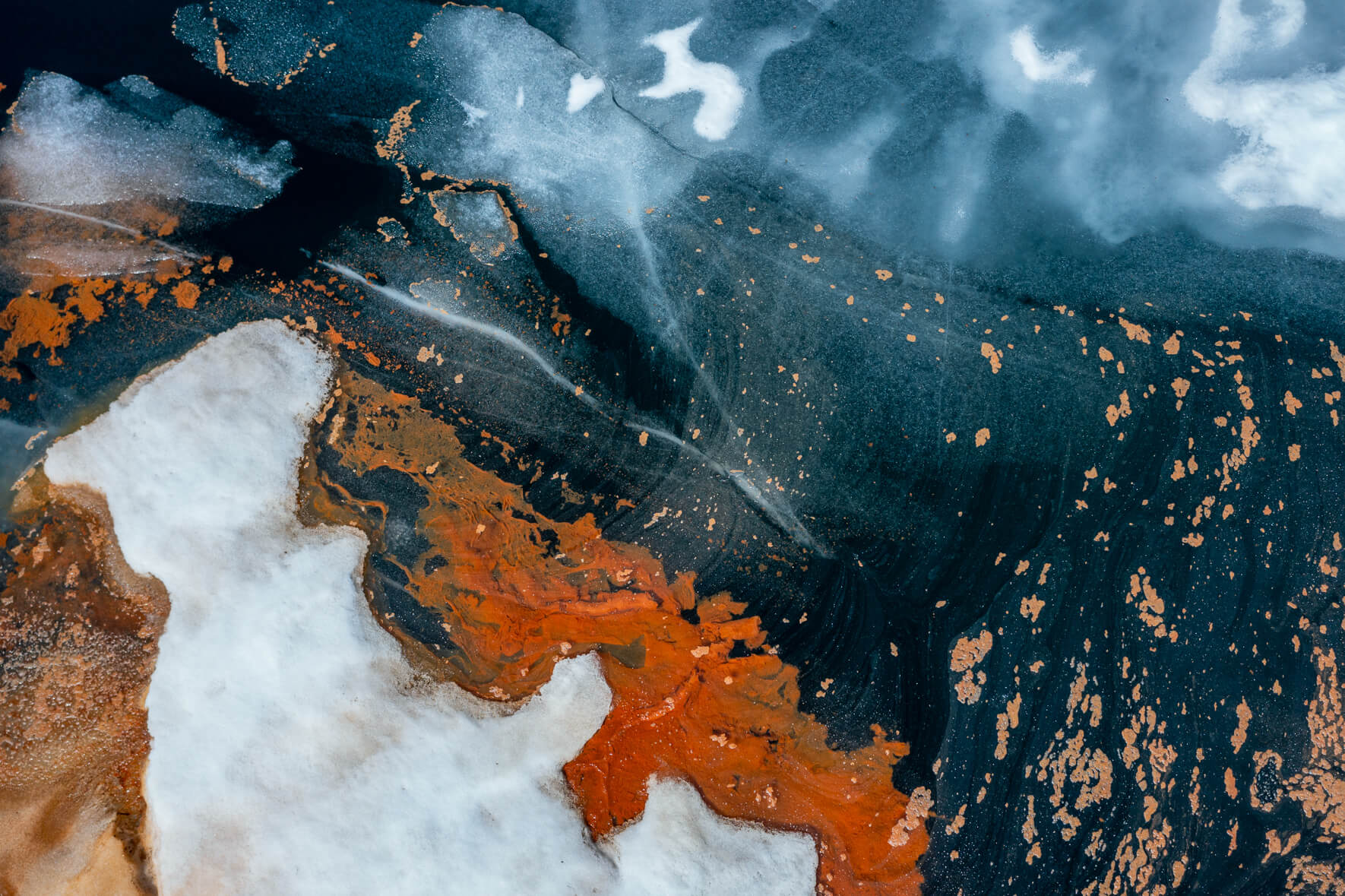 Aerial view of a thawing lake in Norway with cracked ice surface and remnants of snow as well as red pollen