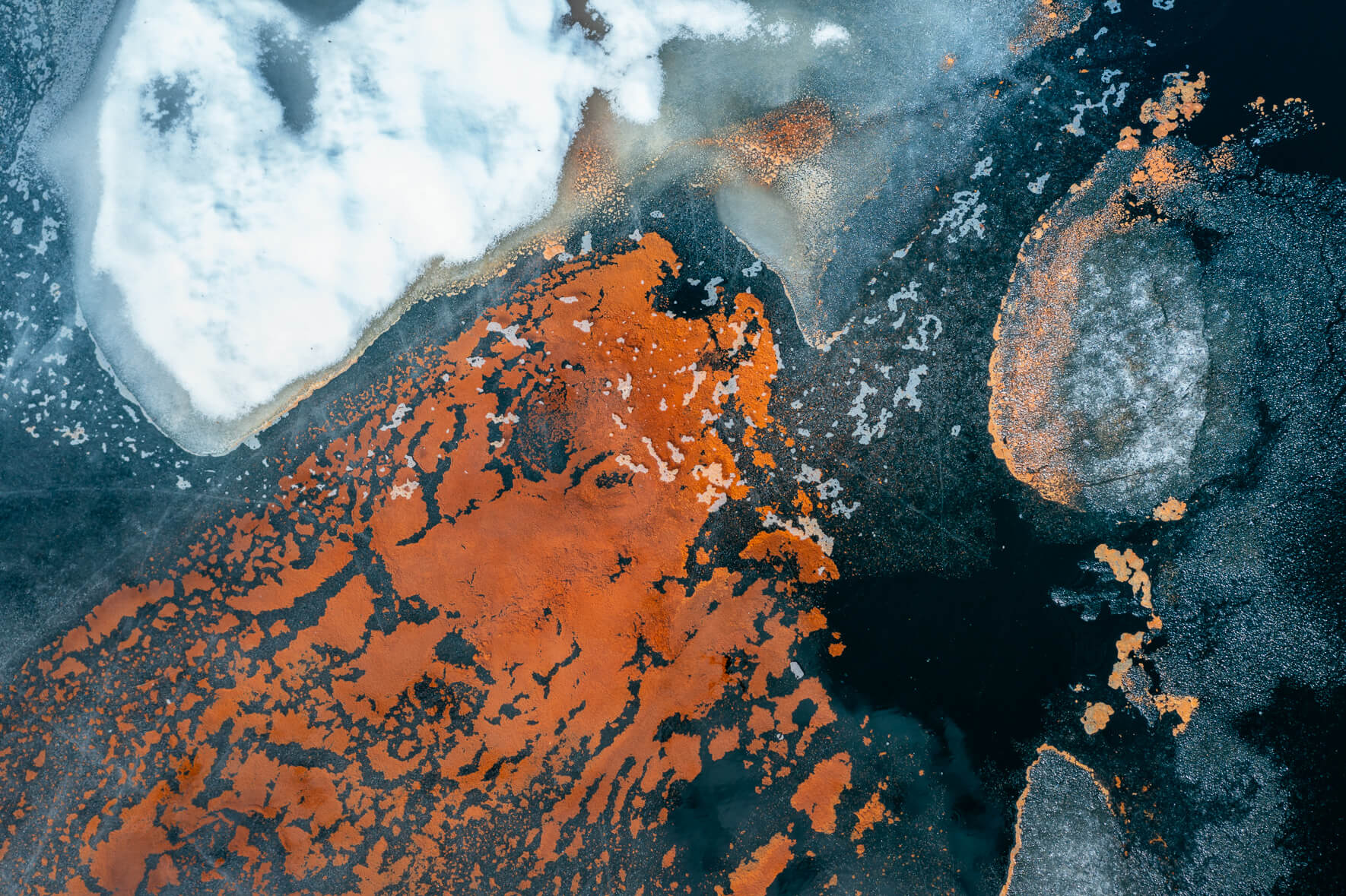 Abstract aerial view of a thawing lake with cracked ice surface and remnants of snow as well as red pollen