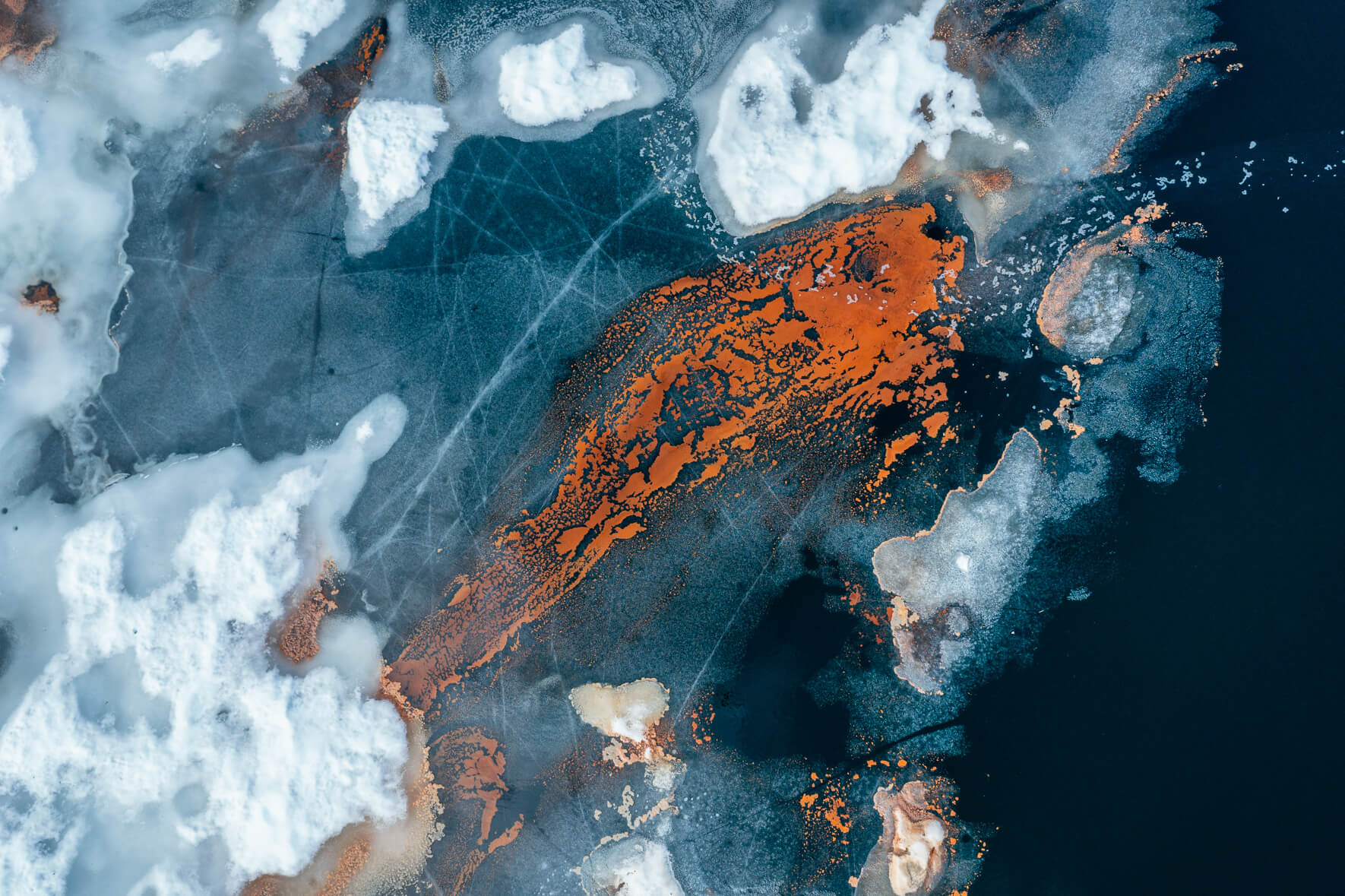 Aerial view of a thawing lake in Norway with ice floes and red pollen in the shape of a fish