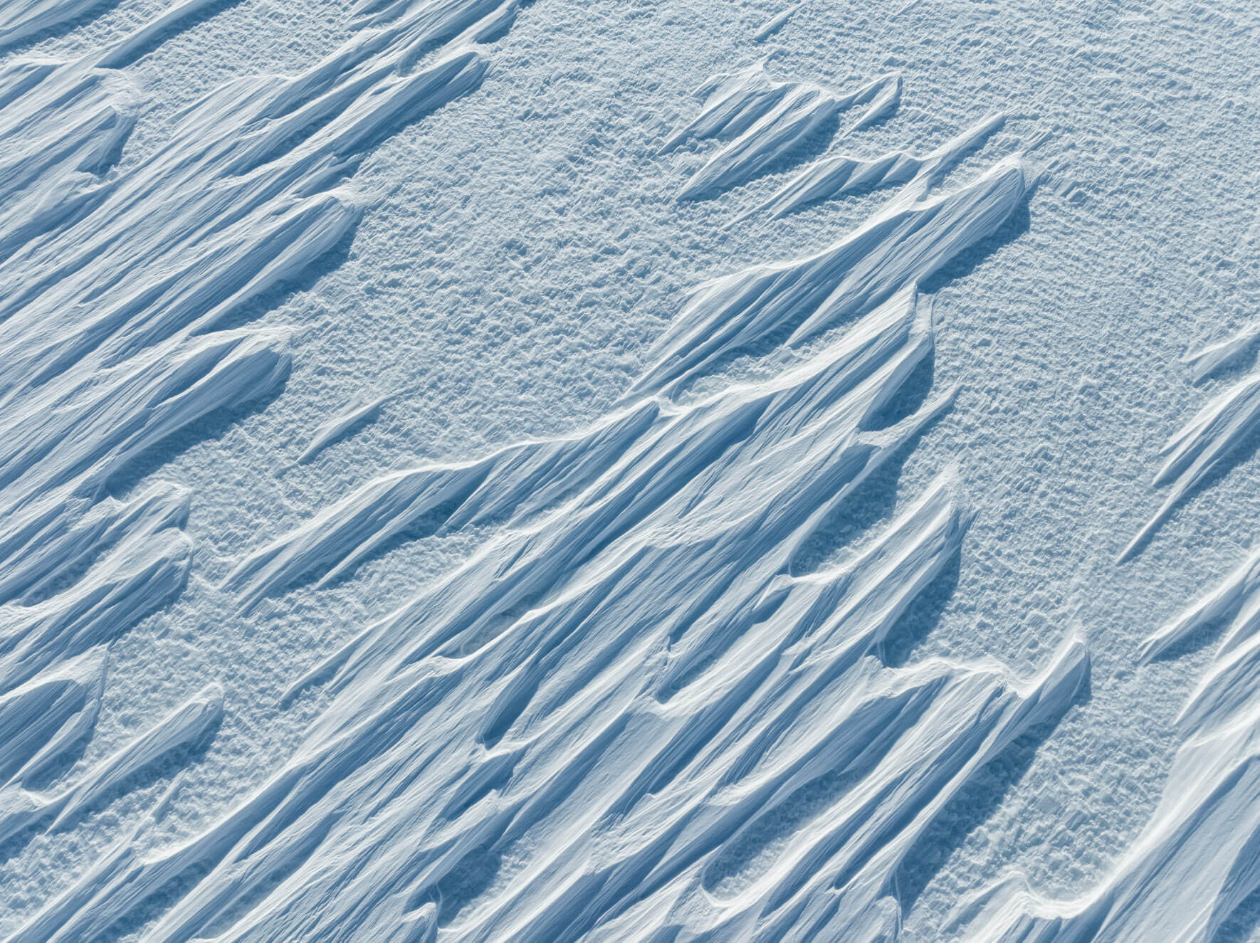 Aerial perspective of wind-sculpted snow formations creating frozen wave-like textures