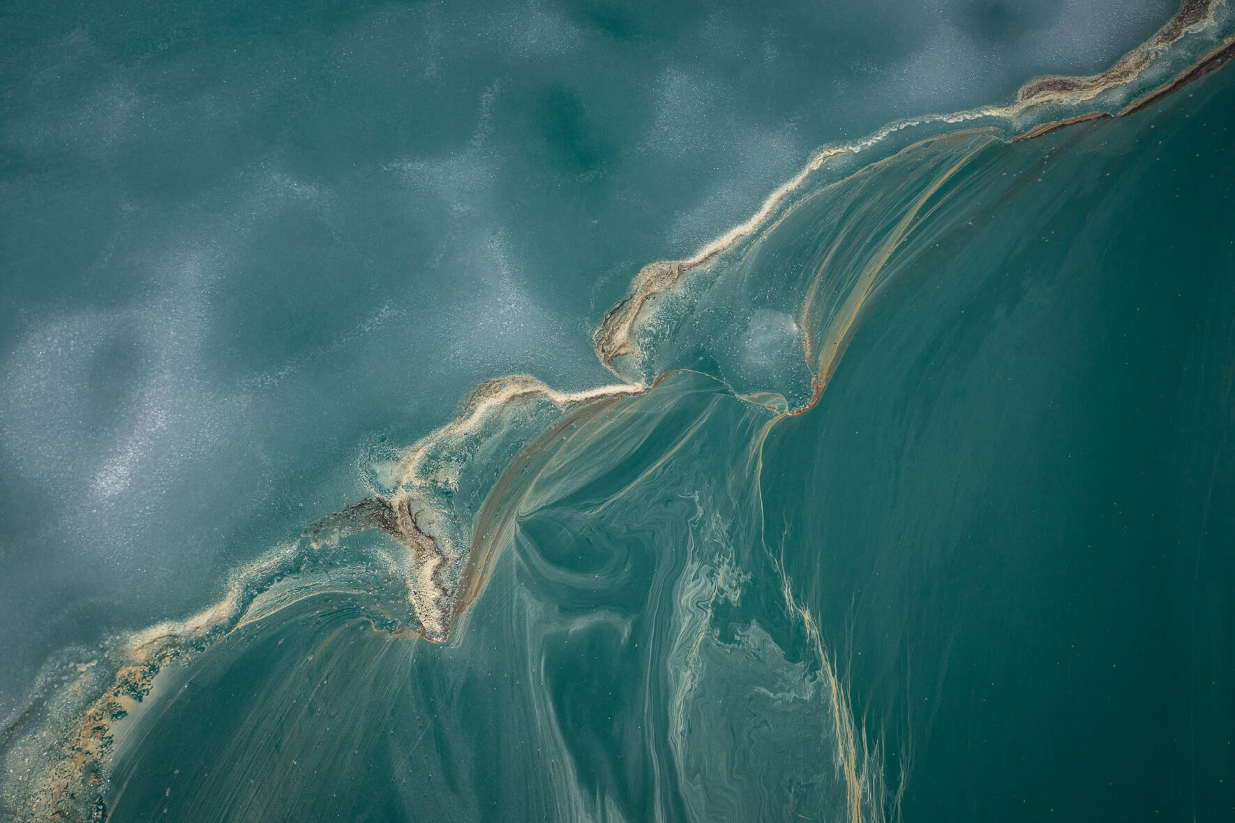 Aerial view of a thawing lake in Norway with remnants of ice and flower pollen forming streaks on the water