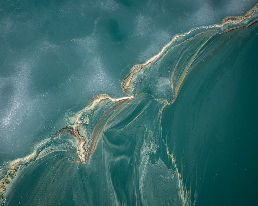 Aerial view of a thawing lake in Norway with remnants of ice and flower pollen forming streaks on the water