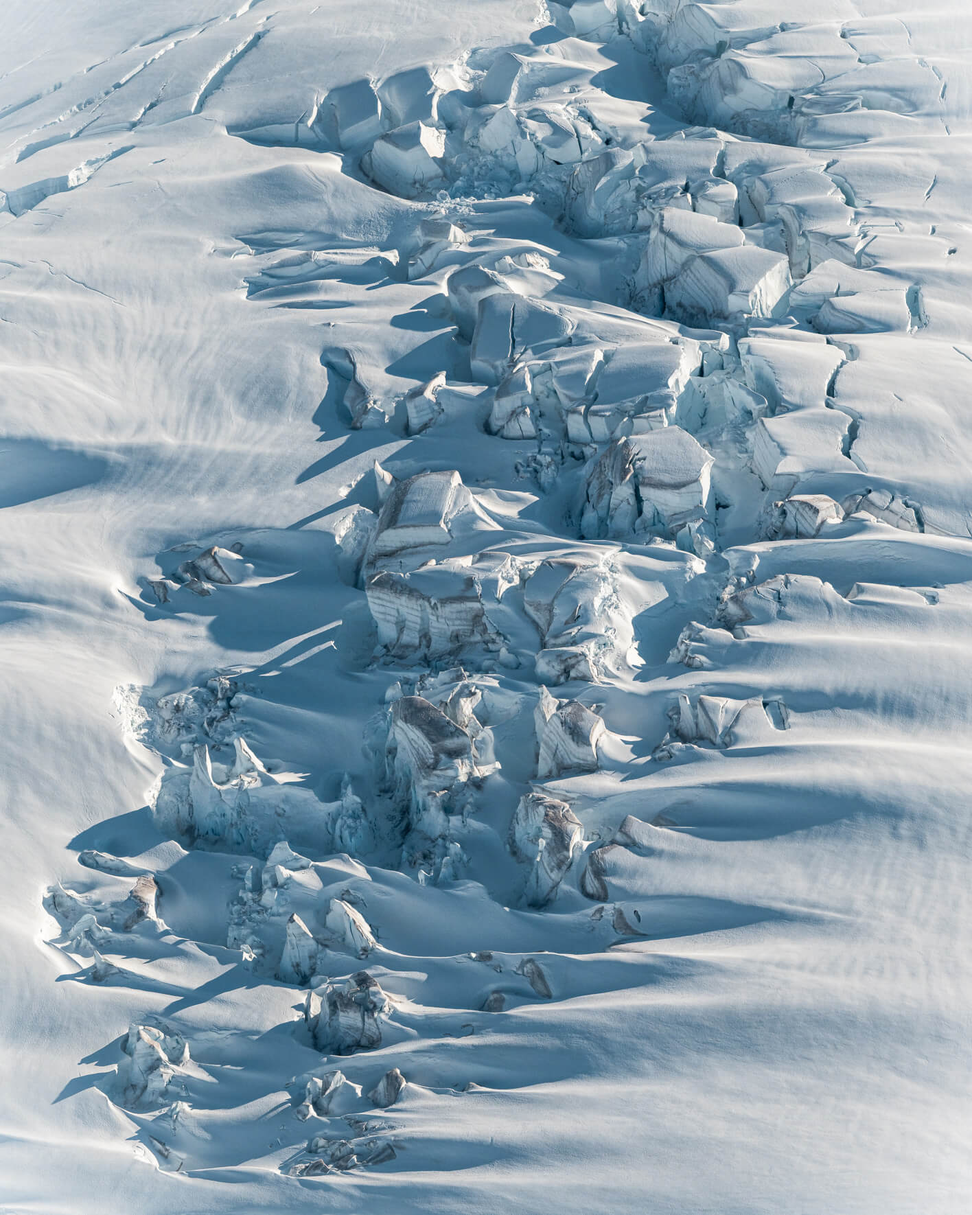 Aerial view of snow-covered glacier surface with elongated crevasses and soft shadows.