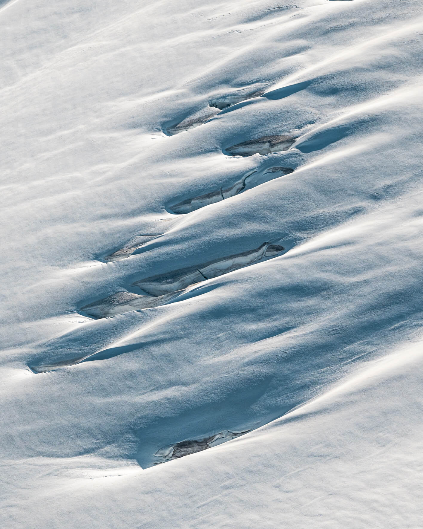 Aerial view of smooth snow formations creating organic wave-like glacier patterns in Alaska