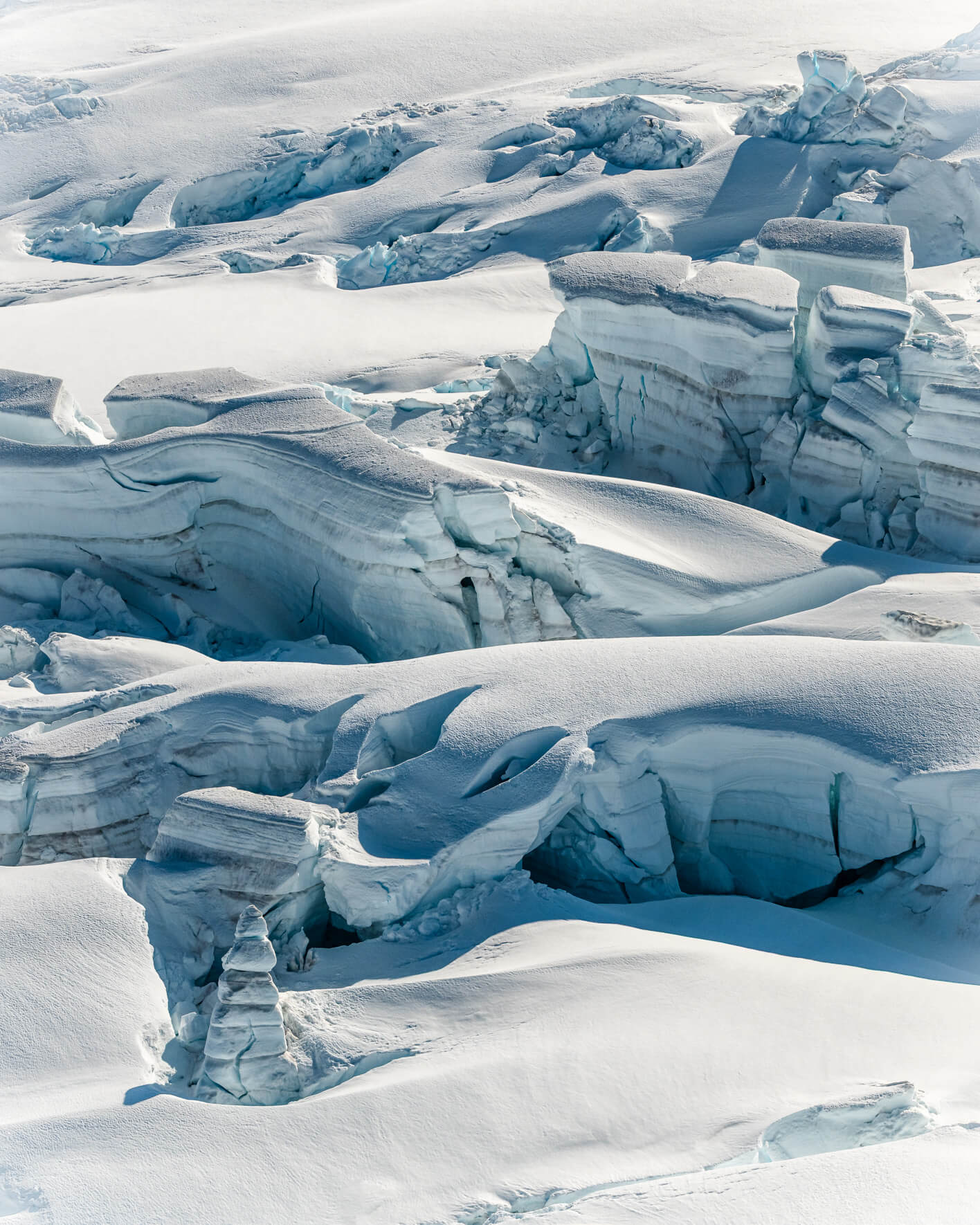 Aerial view of textured glacier ice with intersecting cracks and subtle blue tones.