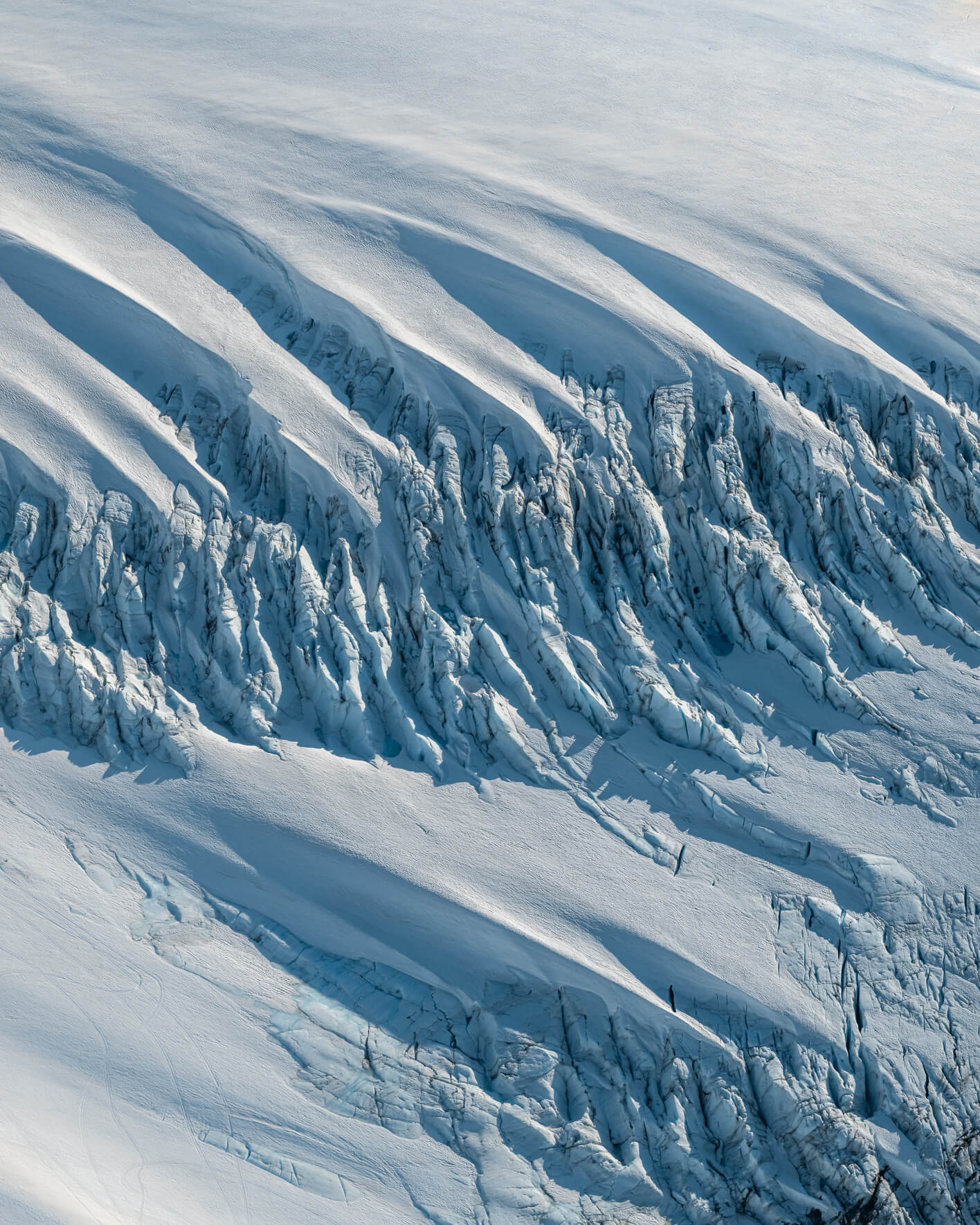 Aerial view of jagged glacier surface with snow-covered ridges and deep crevasses in Alaska