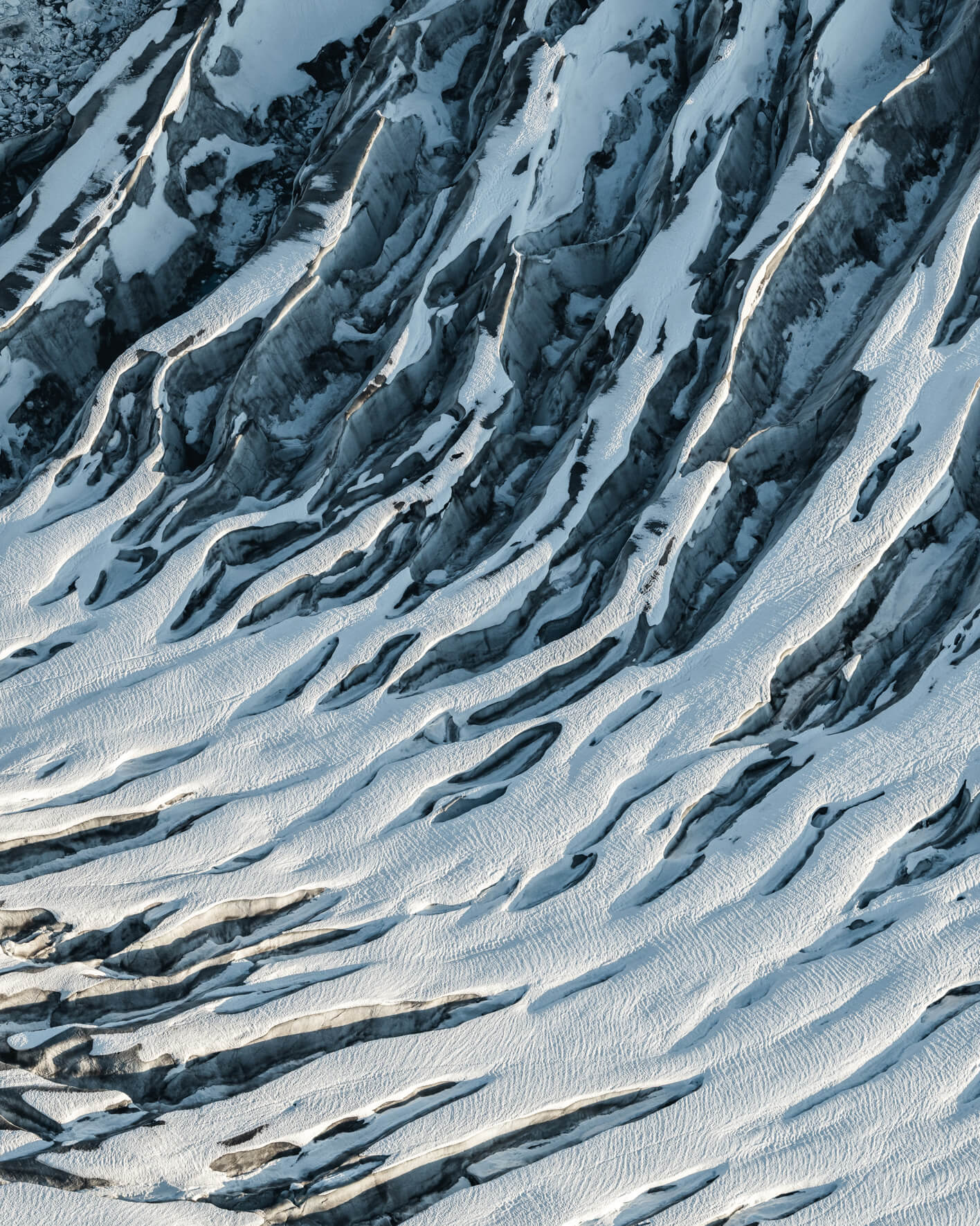 Aerial view of snow-covered glacier surface in Alaska with deep crevasses