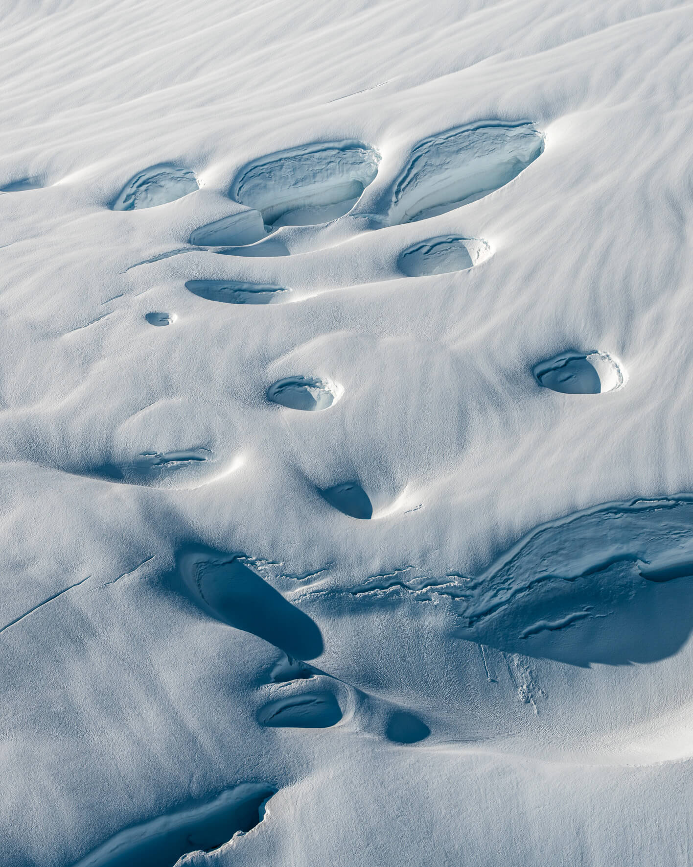 Aerial view of smooth snow formations creating organic wave-like glacier patterns