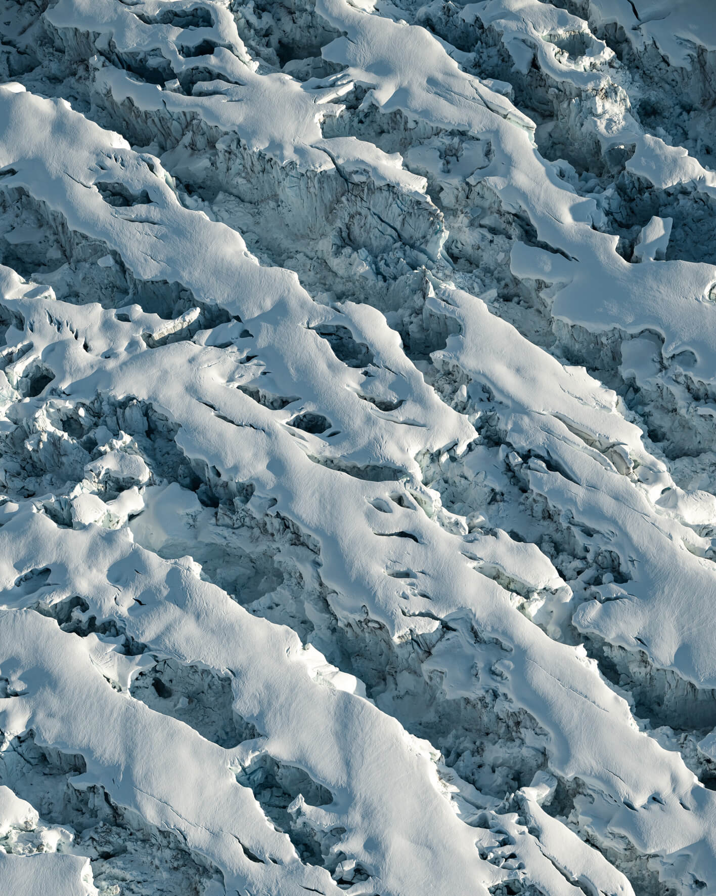 Aerial view of fractured glacier surface with broken ice blocks and sculpted snow