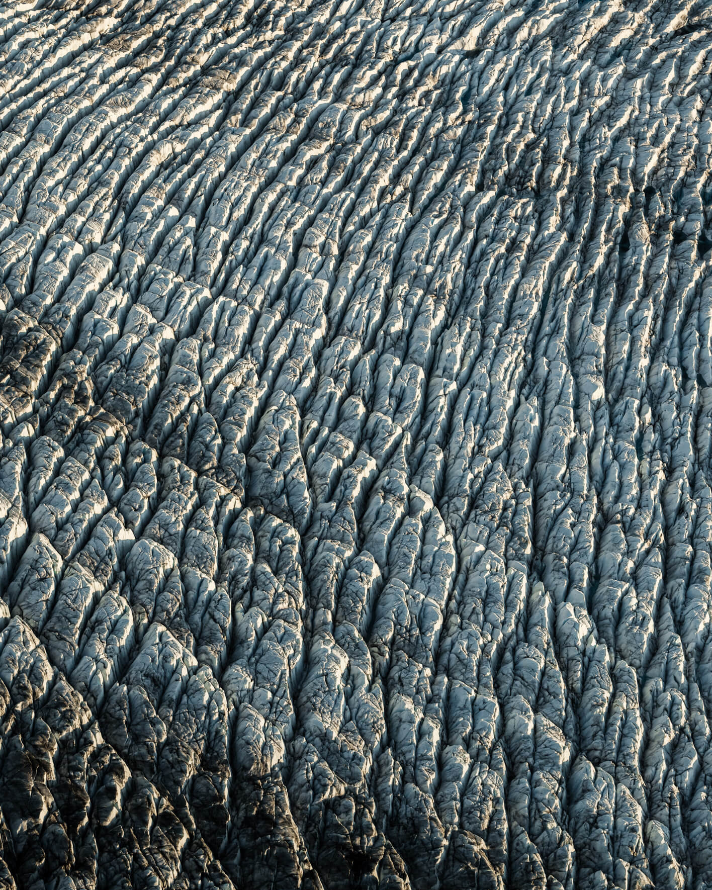 Aerial view of jagged glacier surface with snow-covered ridges and deep crevasses.