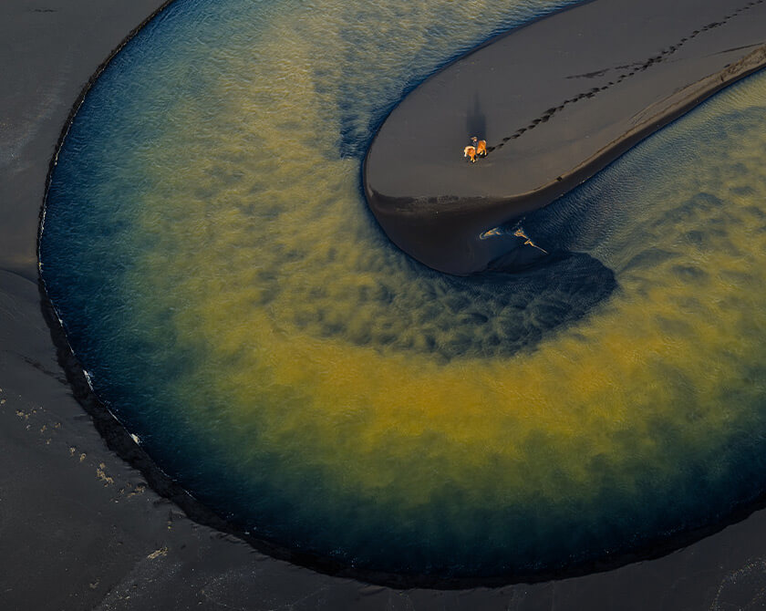 Aerial view of horse on black sand island in Iceland surrounded by glacial river flow