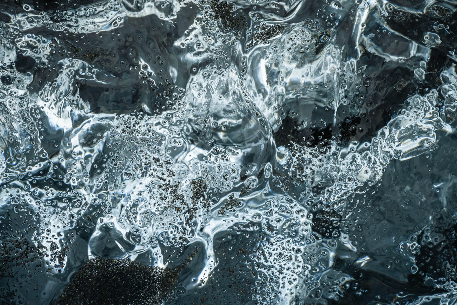 Detail of melting iceberg on volcanic sand with soft reflections of Arctic light