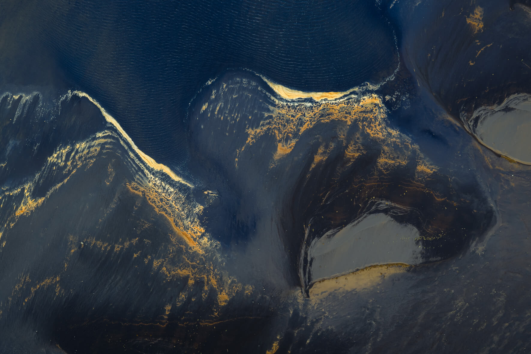 Detail view of lagoon with golden foam patterns on dark sand and deep blue water