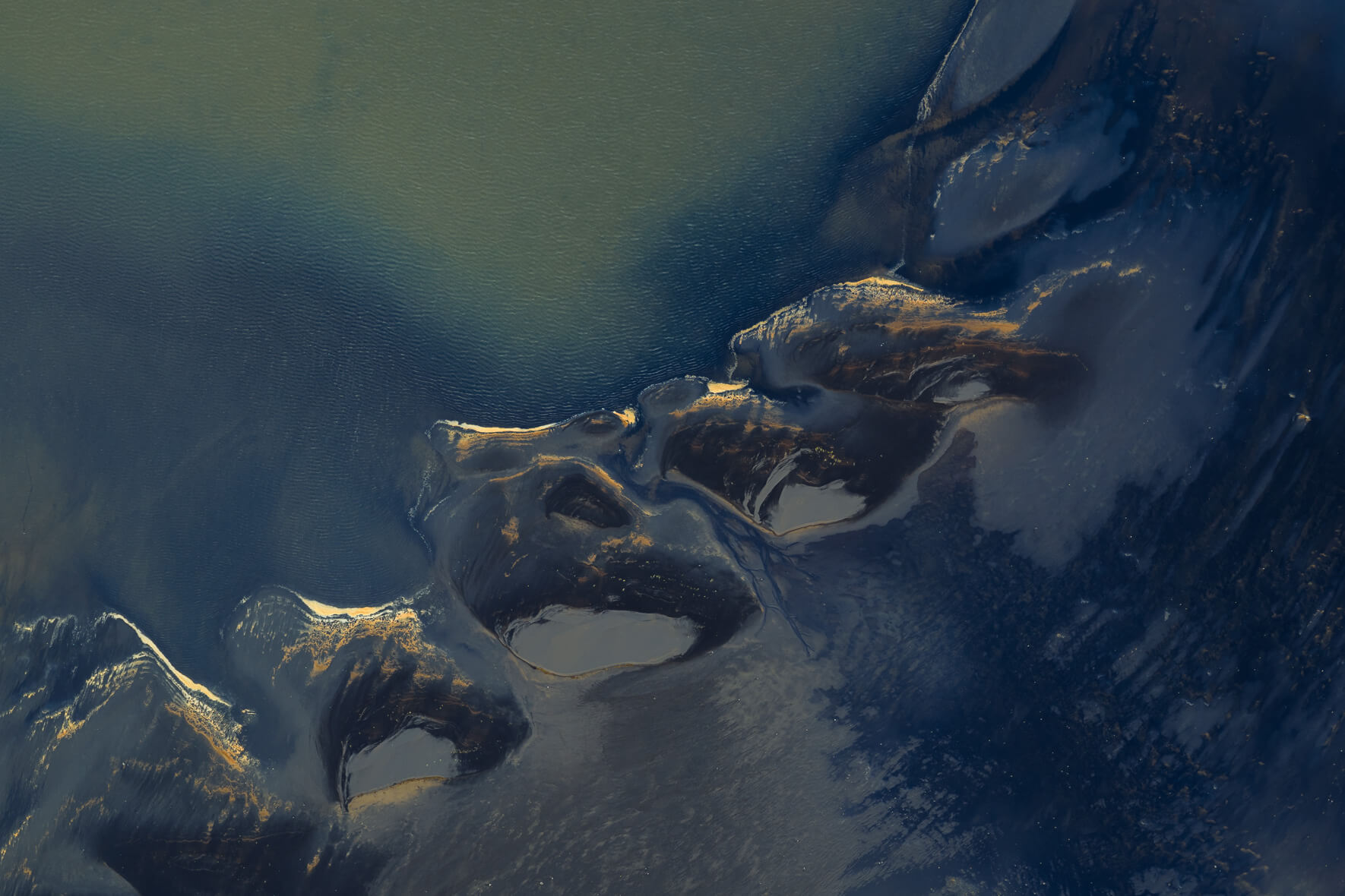 Aerial view of lagoon in Iceland with orange foam patterns on dark sand and deep blue water