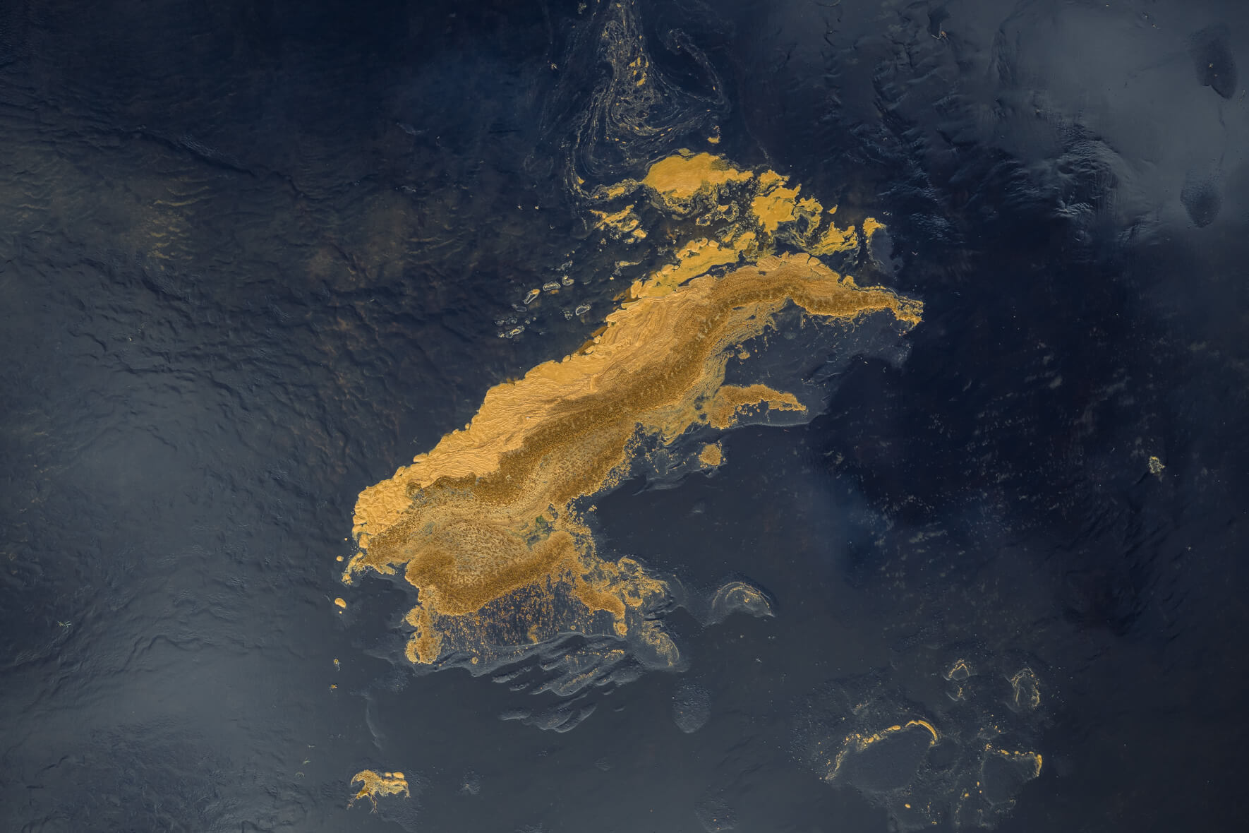 Icelandic lagoon with golden foam traces curve across deep blue tidal water