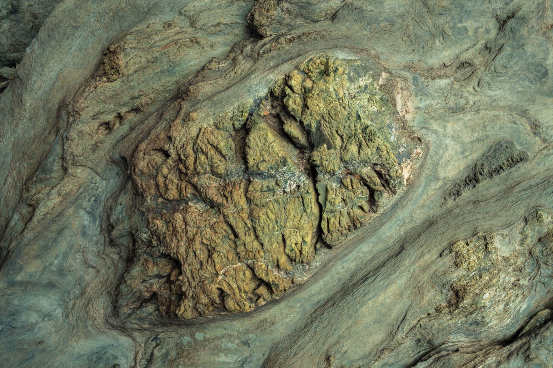 Folded metamorphic rock with greenish hues and oxidized mineral veins